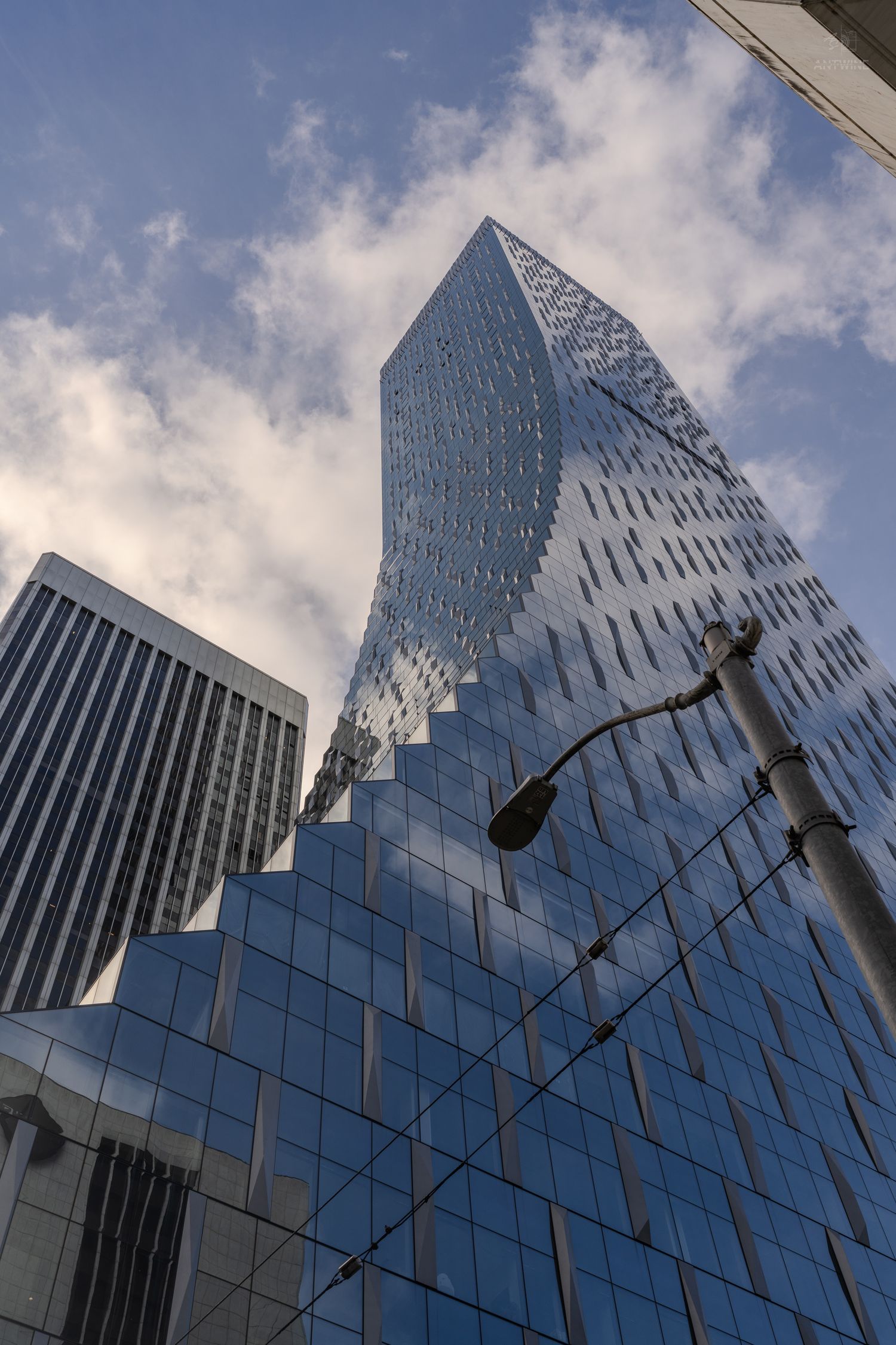 Dramatic low angle view of modern glass skyscraper with twisted facade reflecting cloudy sky.