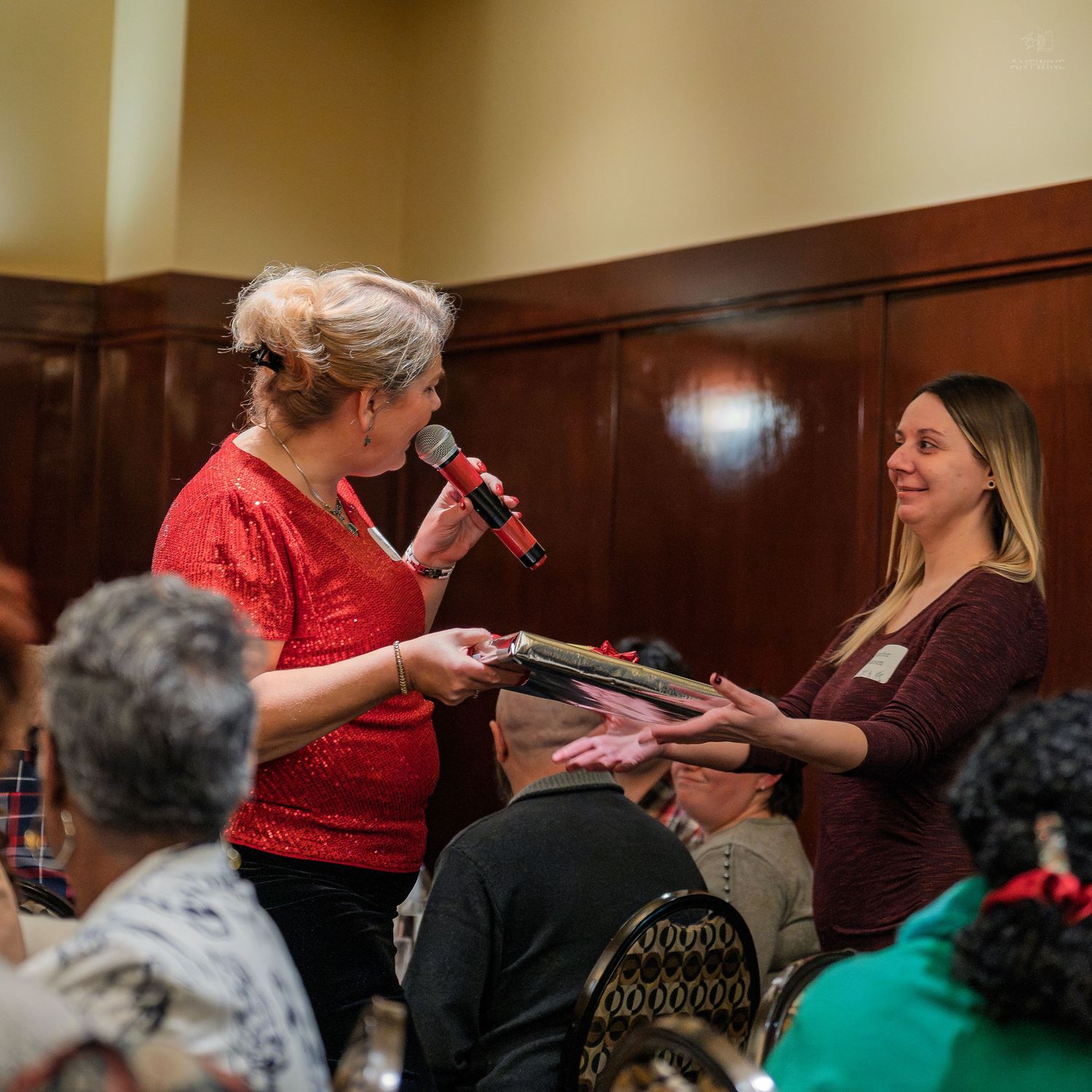 Woman in red top presenting award to another woman at a formal gathering.