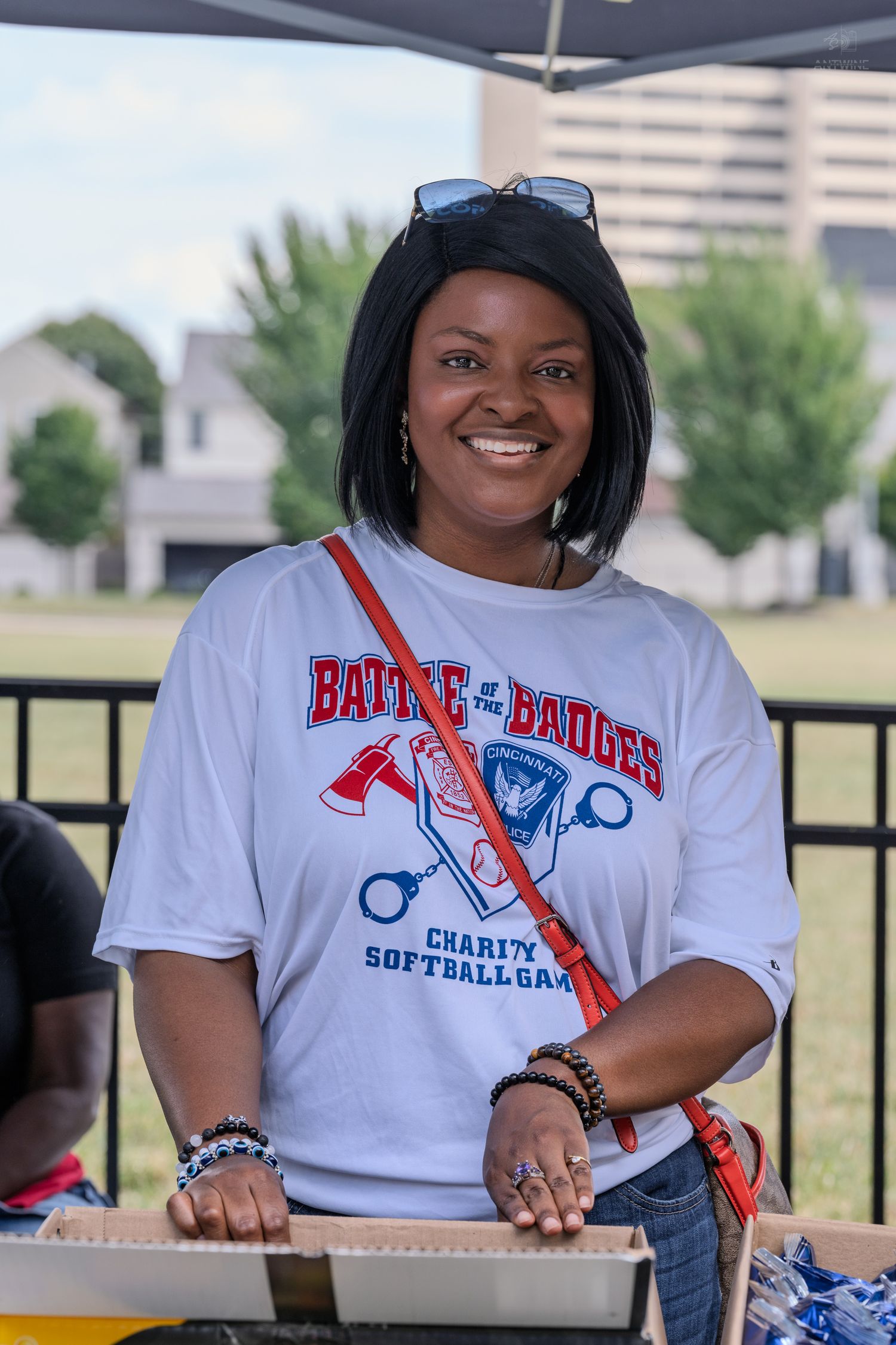 Smiling woman wearing a Battle of the Badges Charity Softball Game white t-shirt at an outdoor event.