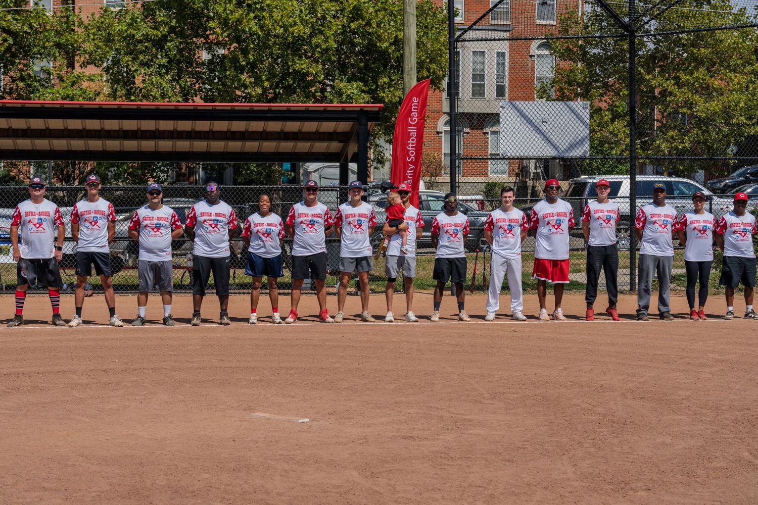 Baseball team in matching white and red uniforms lines up on dirt field on sunny day.