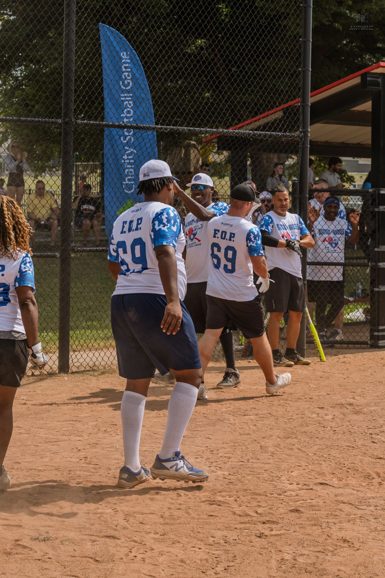 Charity softball game players in matching blue uniforms celebrate near fence with banner.