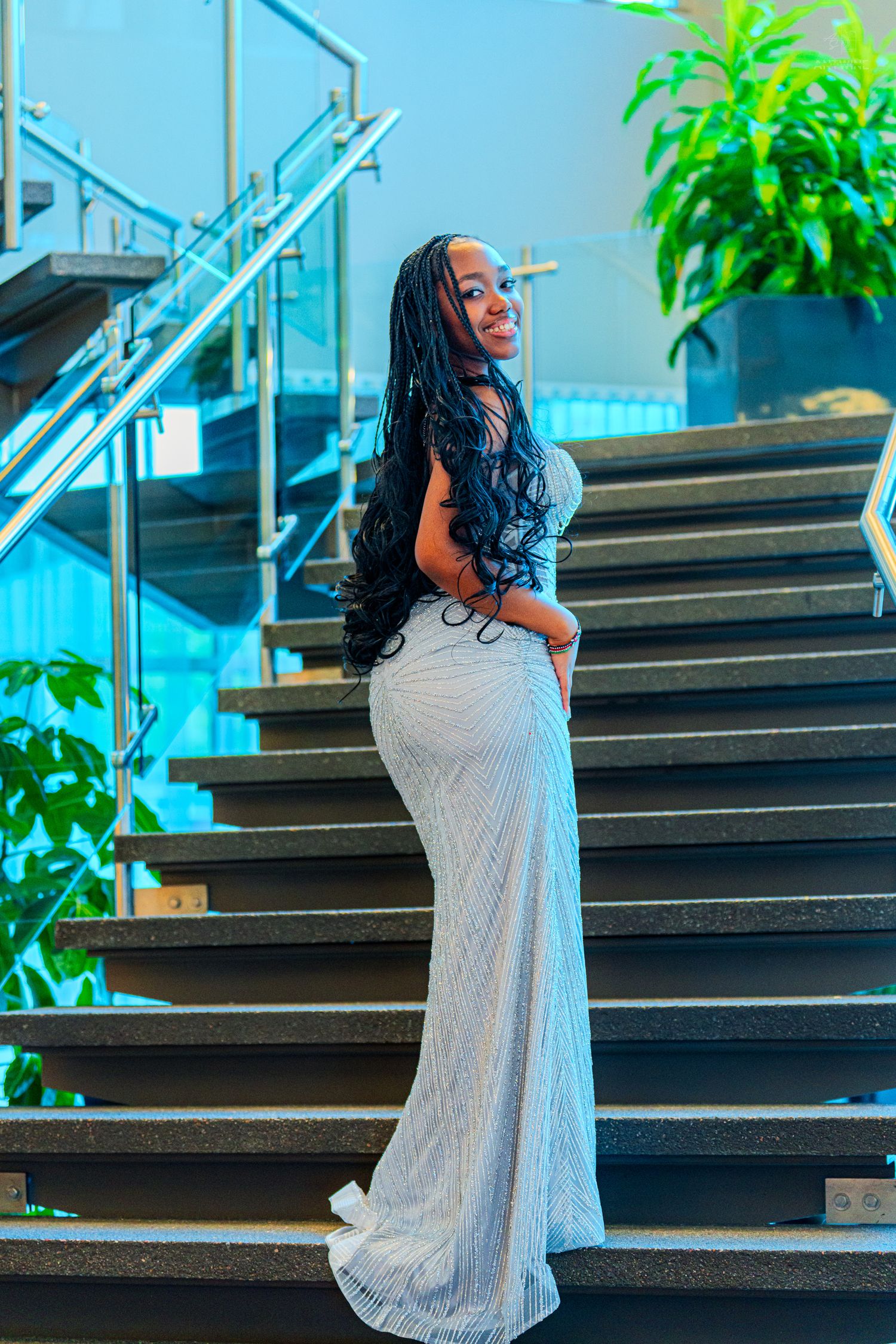 Woman in silver sequin gown posing on stairs with long braided hair.