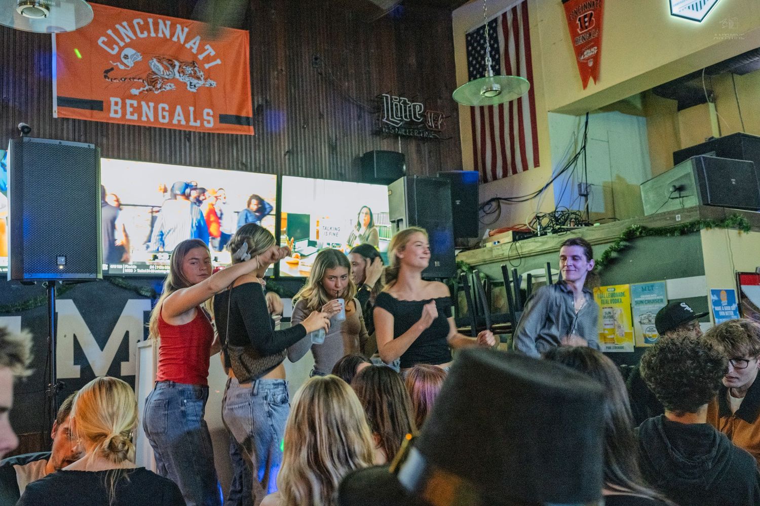 People dancing and socializing inside a bar with a Cincinnati Bengals banner on the wall.