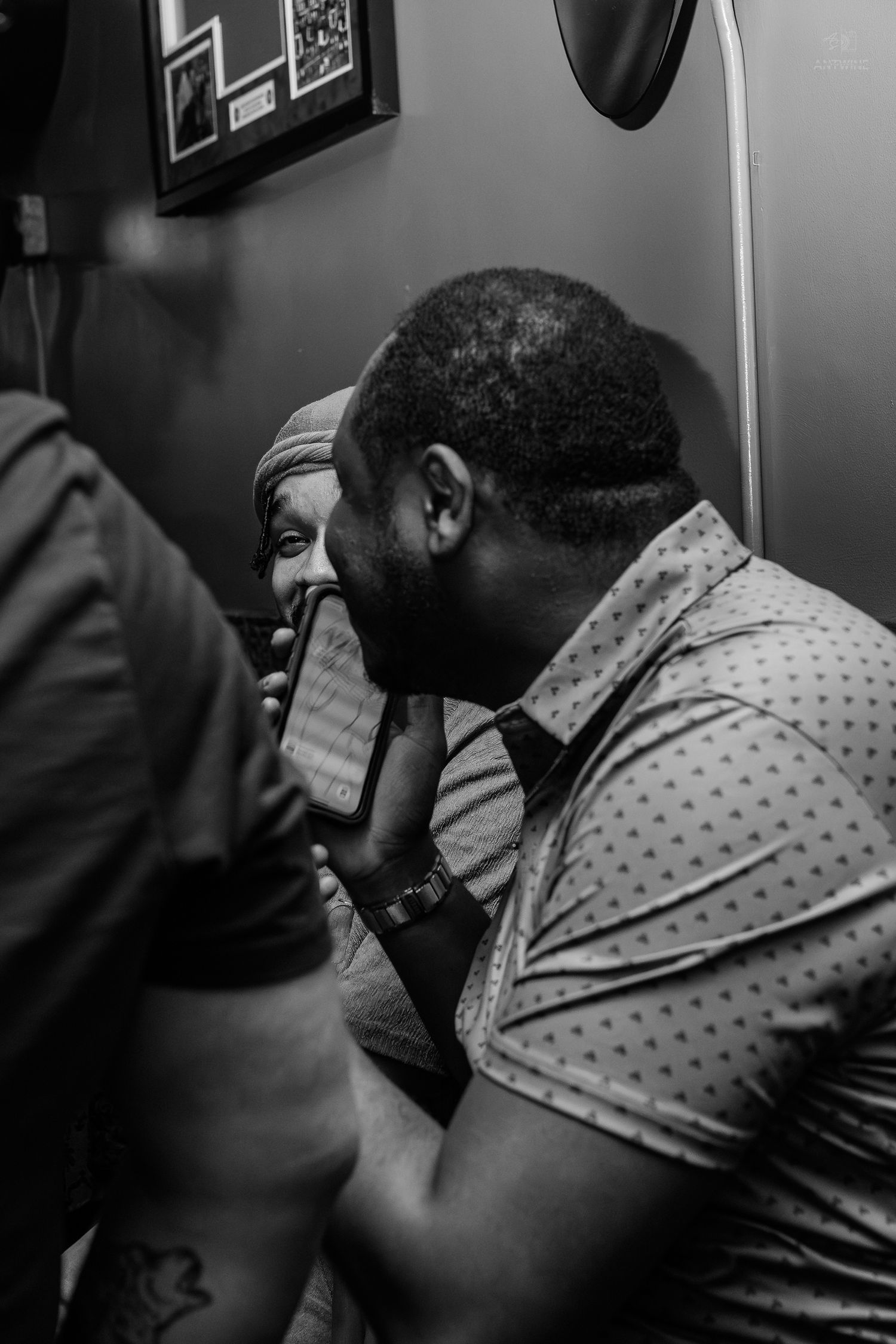 Black and white photo of two men in close conversation at an indoor gathering, one whispering to the other.