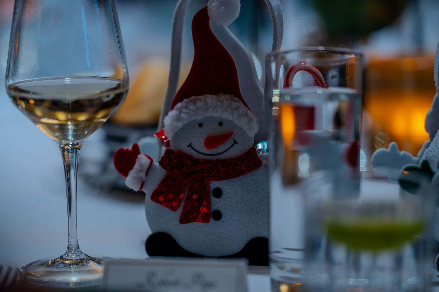 Festive snowman decoration on a holiday table with wine glass and candles in soft evening light.