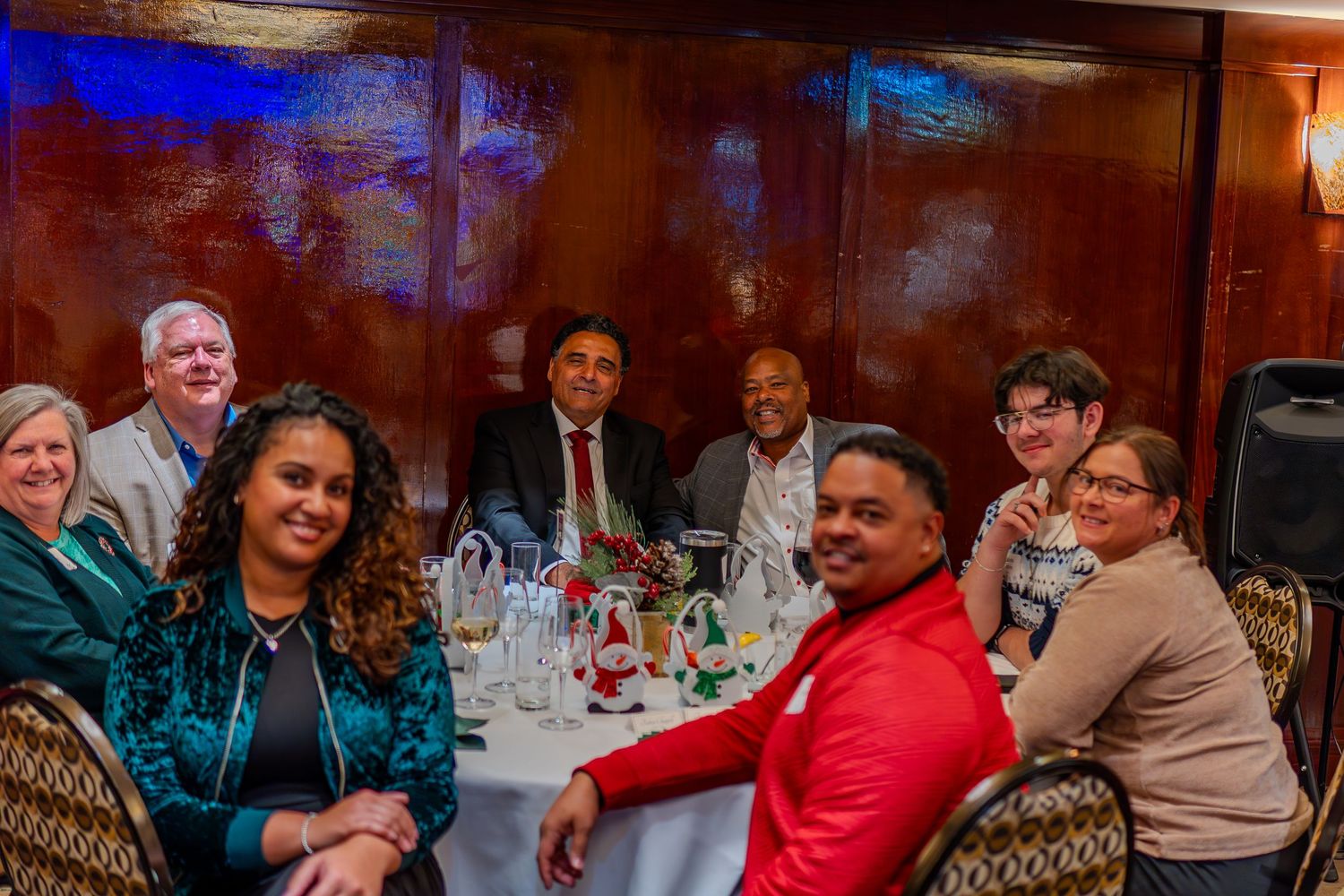 Group of diverse professionals smiling at a formal dinner table with white tablecloth and festive decorations.