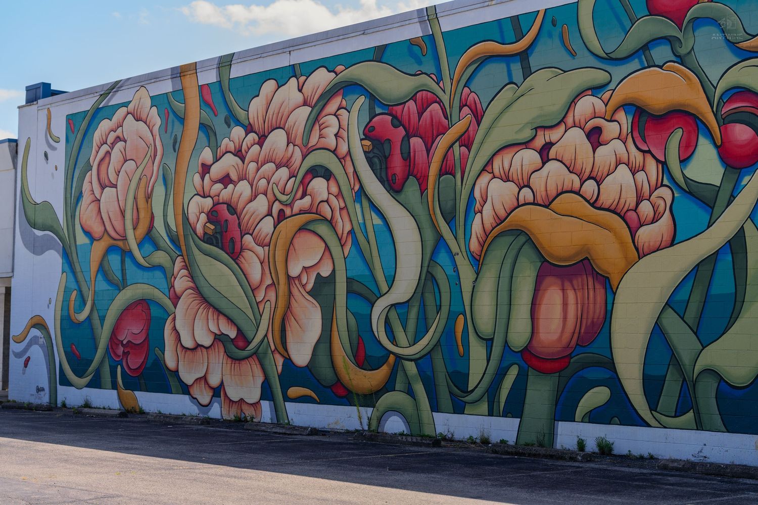 Vibrant street mural featuring large colorful peony flowers with swirling green vines on a building exterior wall.