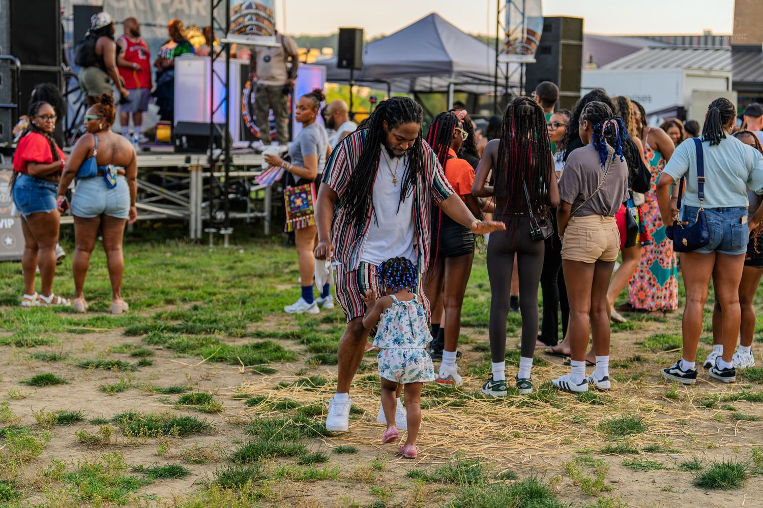 Adult and child dancing together at an outdoor Juneteenth festival on a grassy area near a stage.