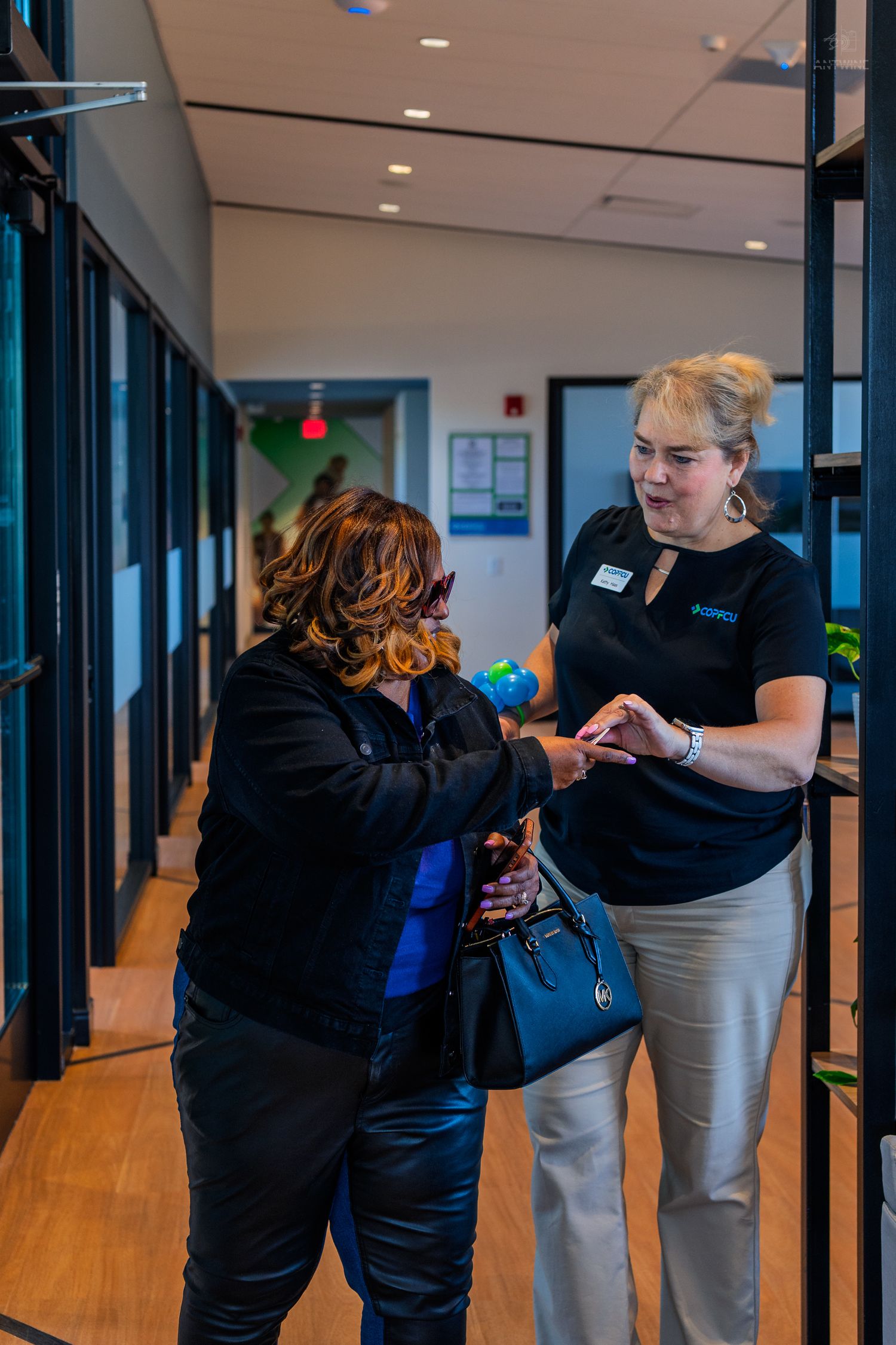 A staff member in a black uniform assists a guest in a modern office hallway during a corporate event.