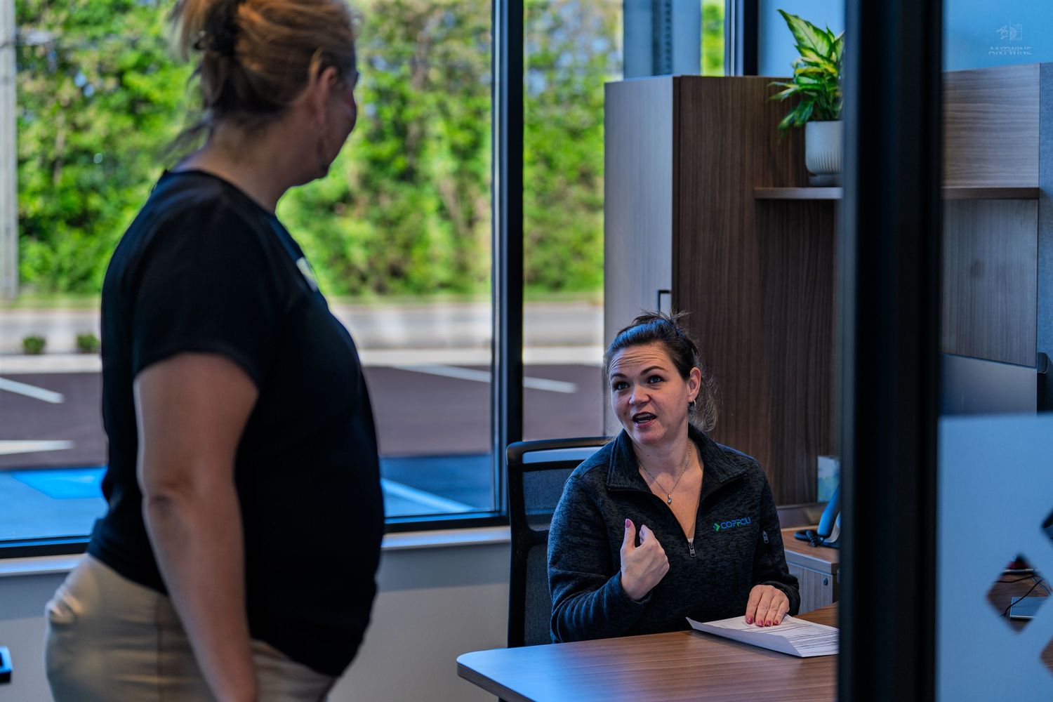 Two women having a conversation at a modern reception desk in a bright office lobby.