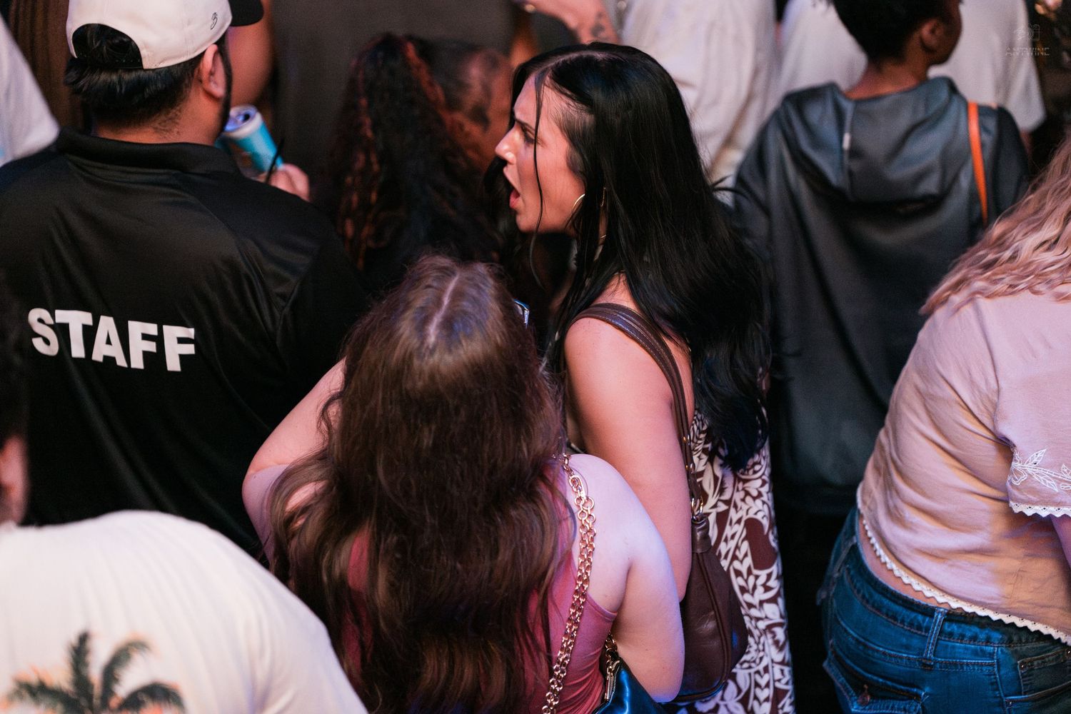 Crowd of partygoers near a staff member in a black shirt at a busy nightclub event.