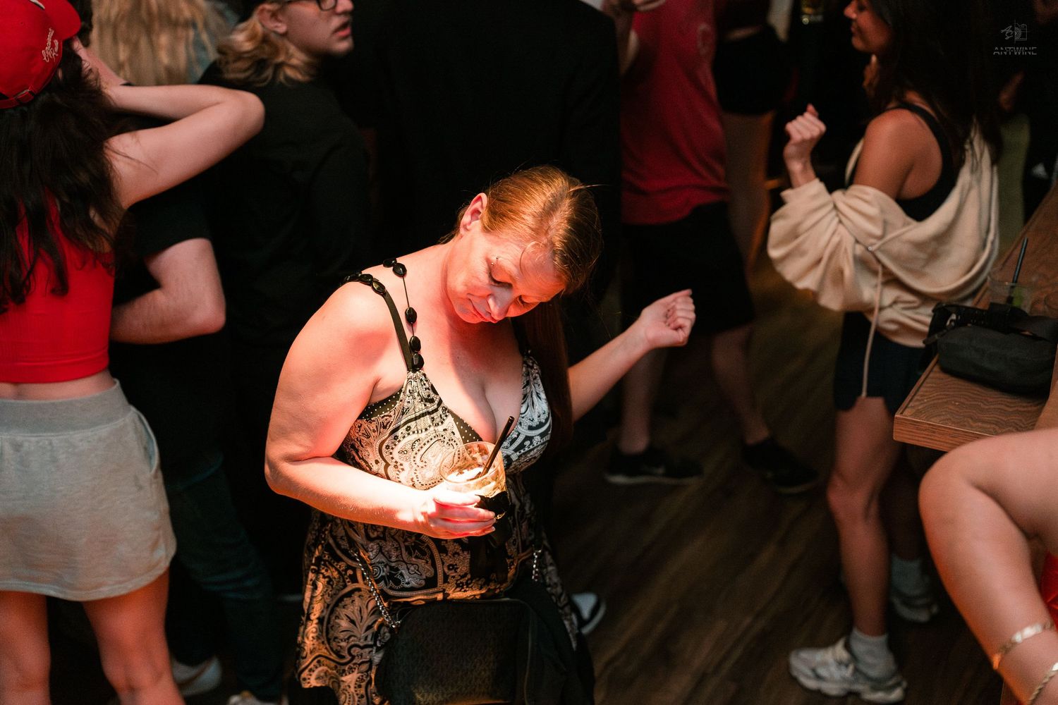 A redheaded woman in a patterned dress dances alone on a crowded nightclub dance floor.