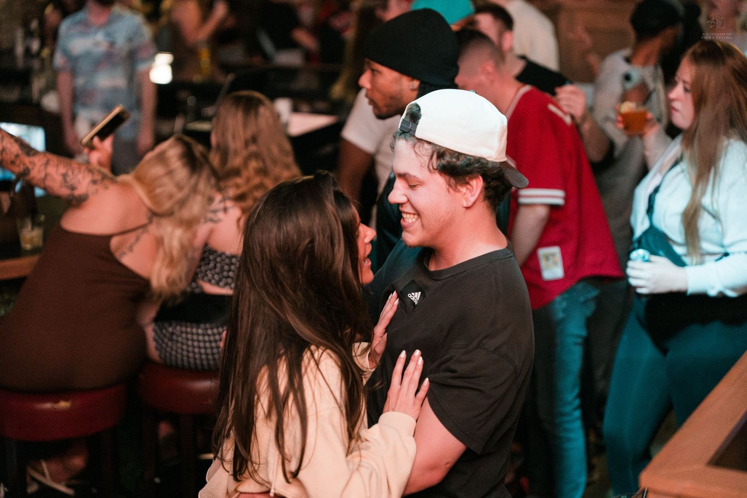 Smiling couple sharing a close moment together at a lively, warmly lit bar.