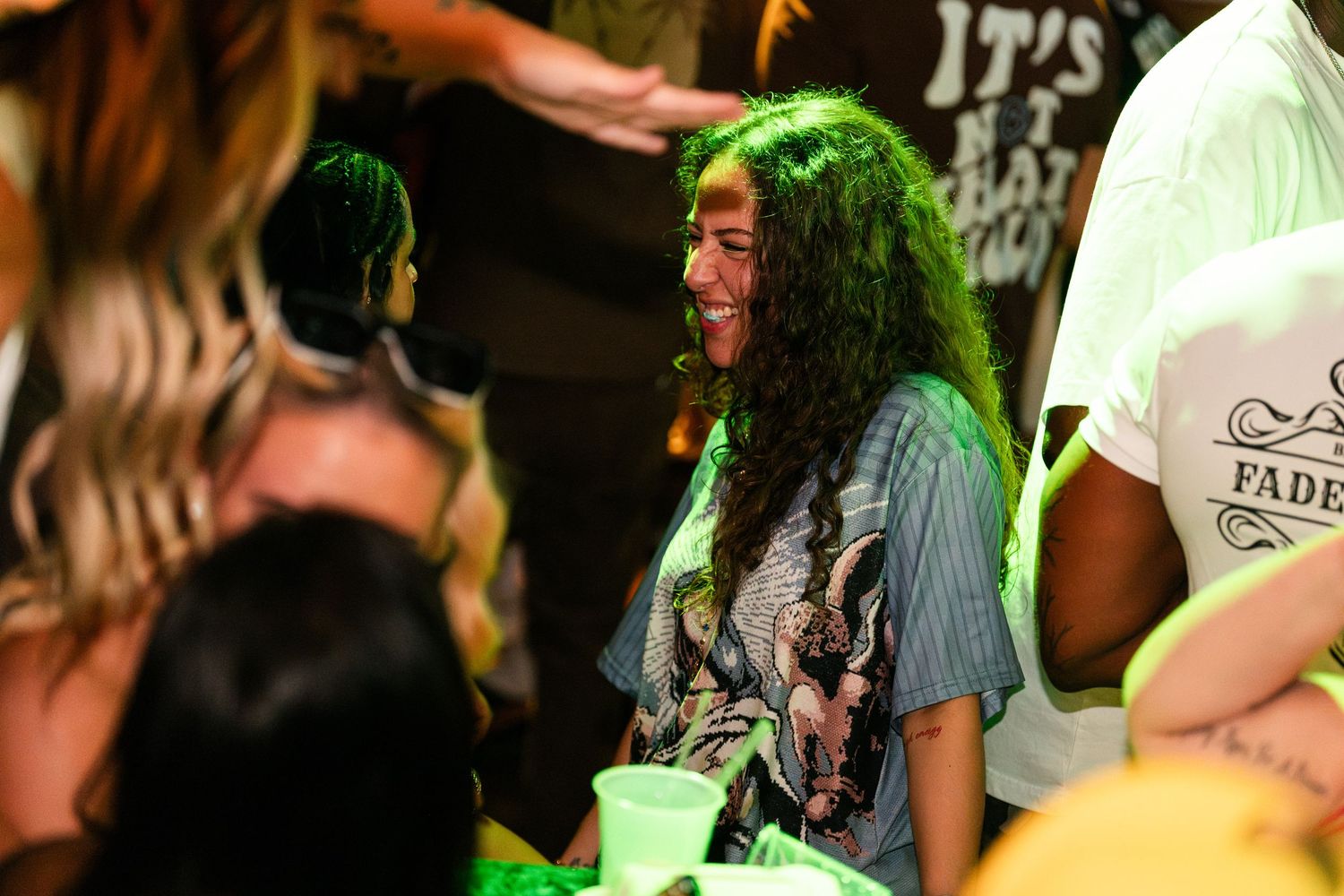 Woman with long curly hair smiling under green lights at a party.