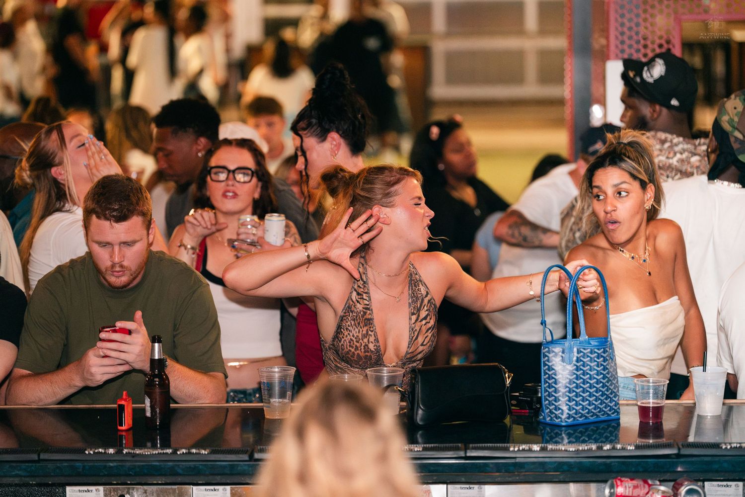 Group of friends reacting with surprise and laughter at an outdoor bar during a nightlife event.