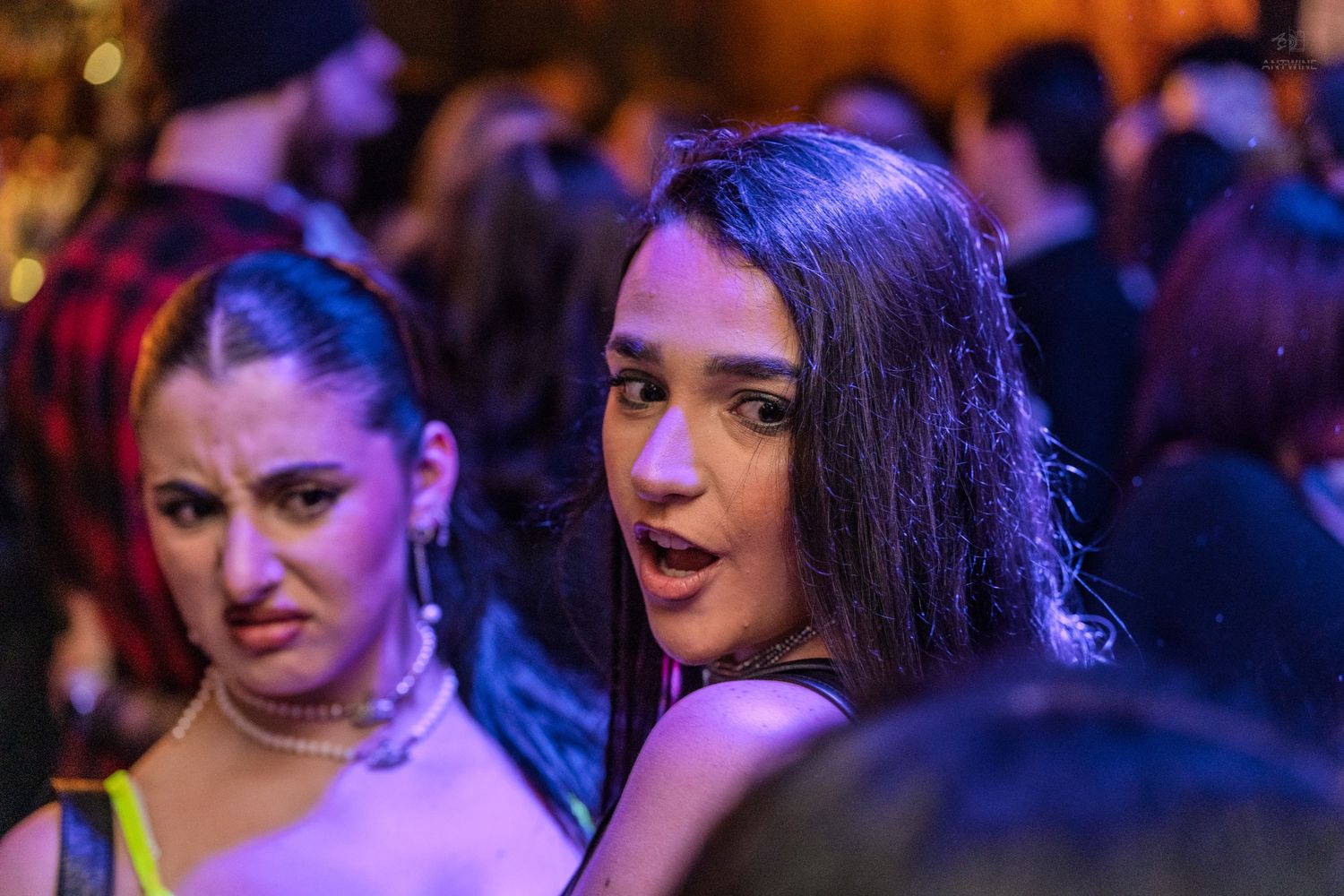 Two women socializing at a vibrant nightclub party with purple lighting.