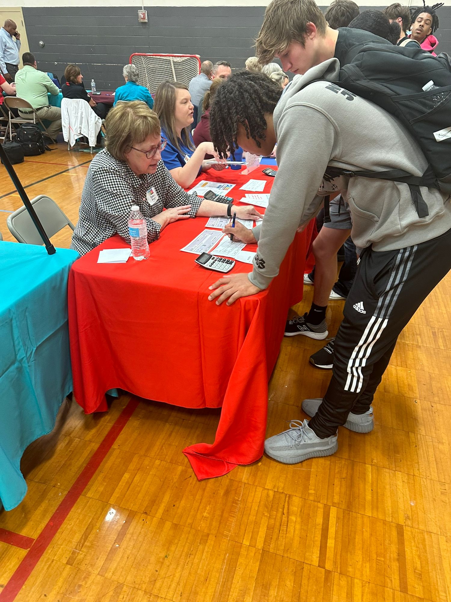 Students interact with a recruiter at a red table during a school job fair in a gymnasium.