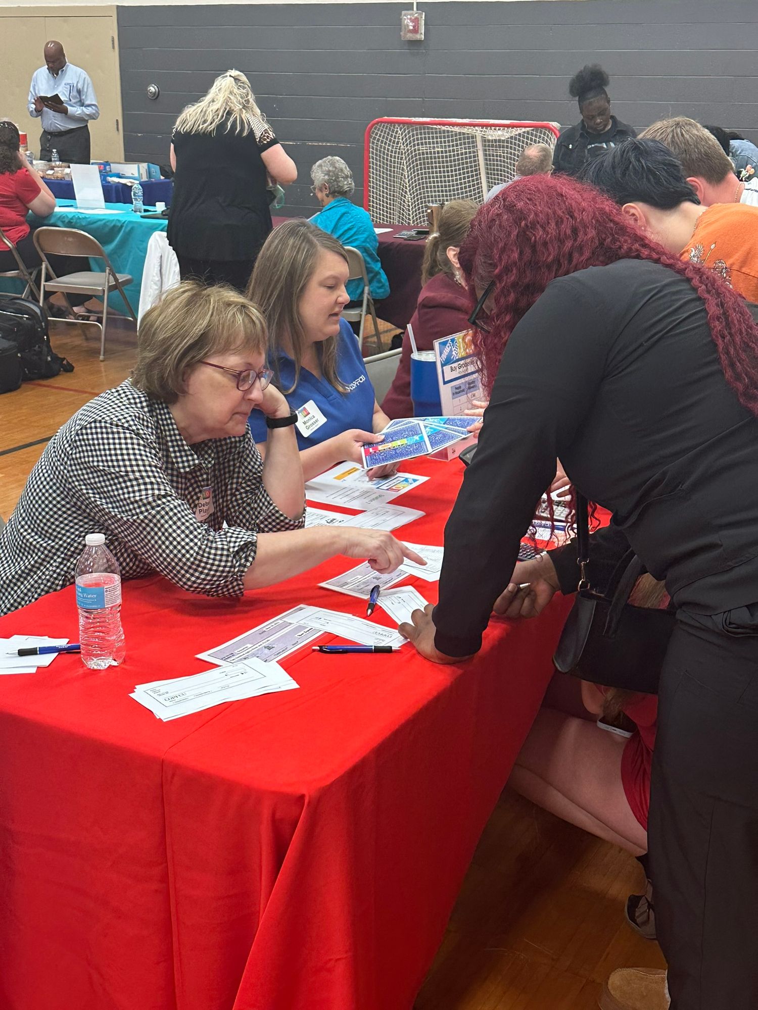 Job fair attendees consulting with recruiters at red table in gymnasium.