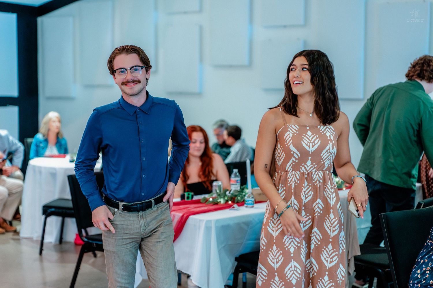 Man in blue shirt and woman in patterned dress smiling at a wedding reception venue.