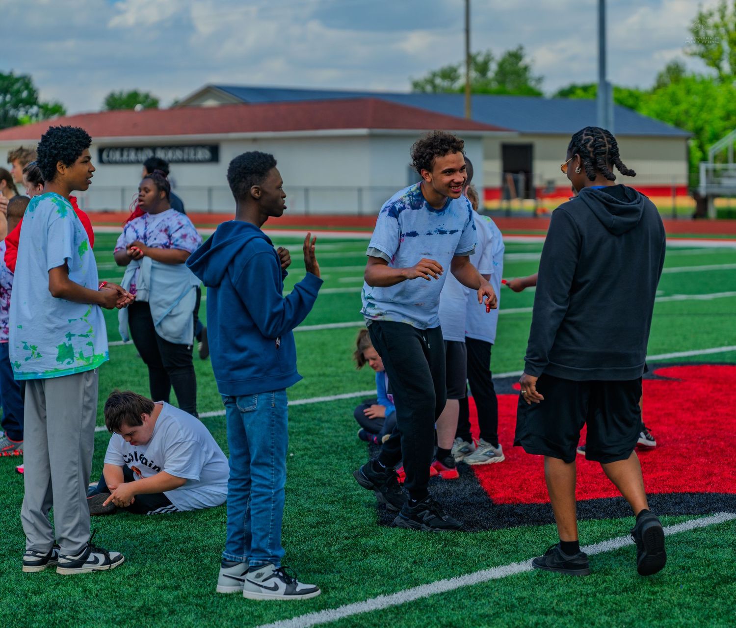 Students socializing on a green turf football field during an outdoor school event on a cloudy day.