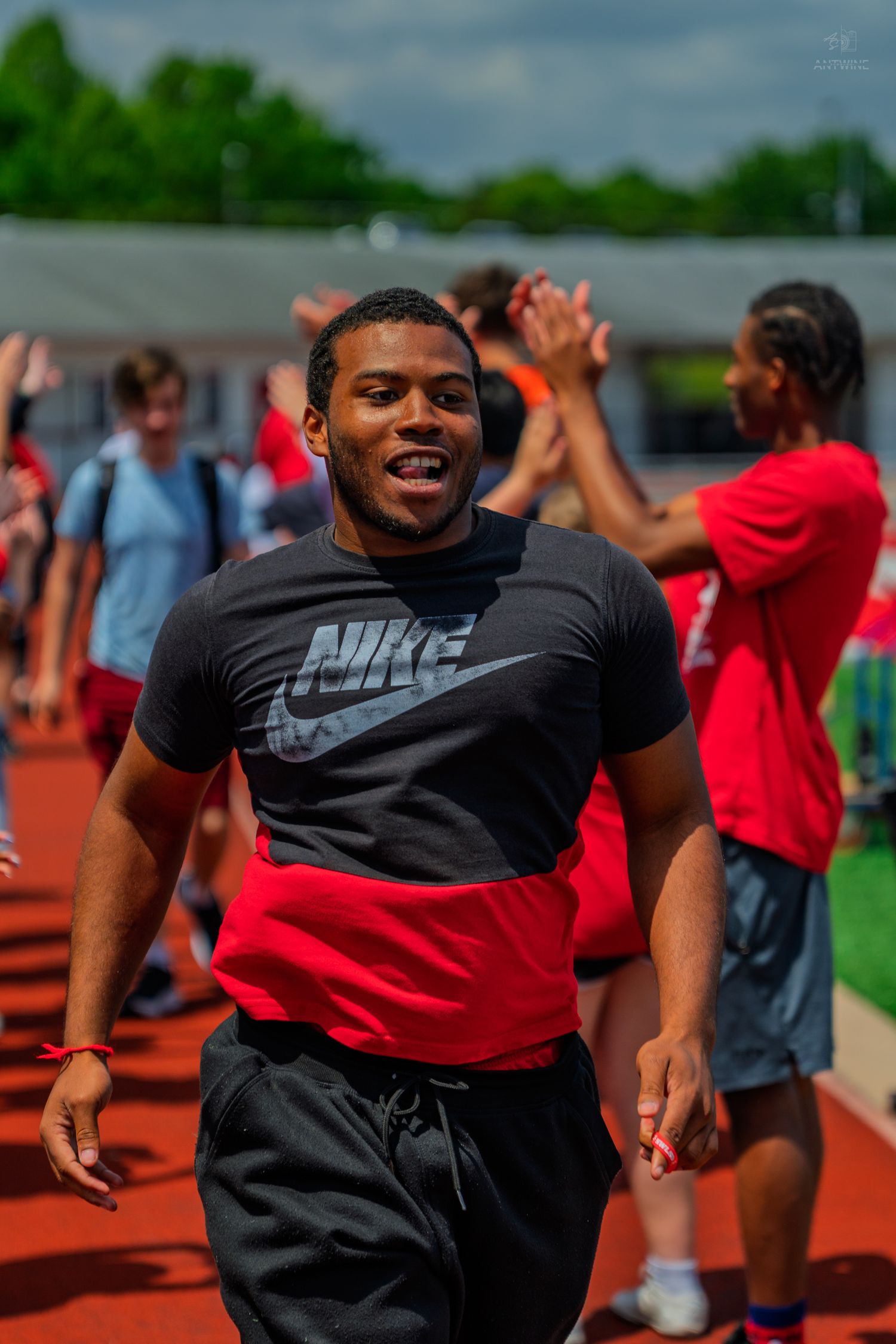 Young man in Nike shirt high-fiving teammates on a red track during an outdoor athletic event.