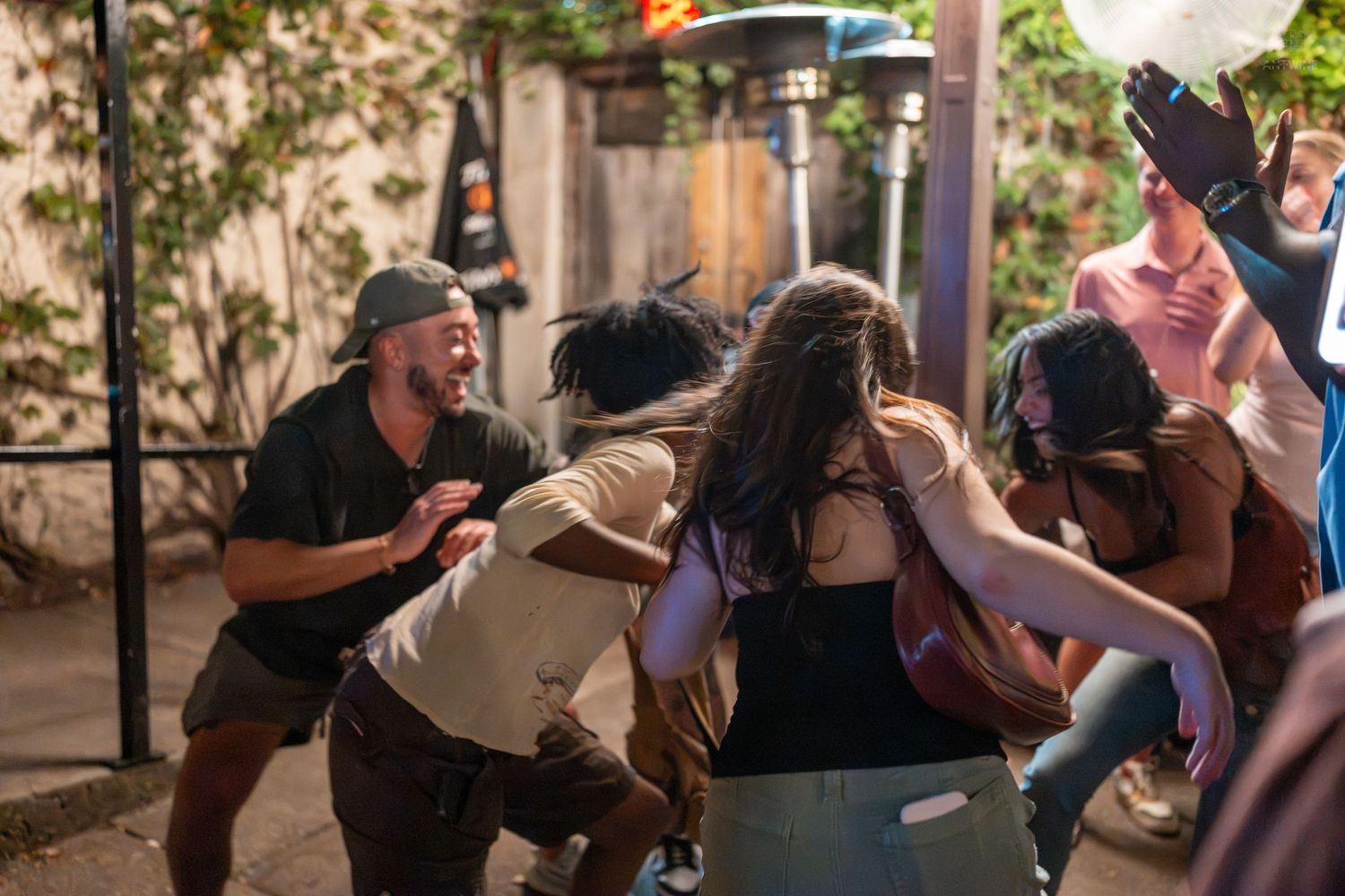 Group of young adults laughing and dancing together at an outdoor evening party event.