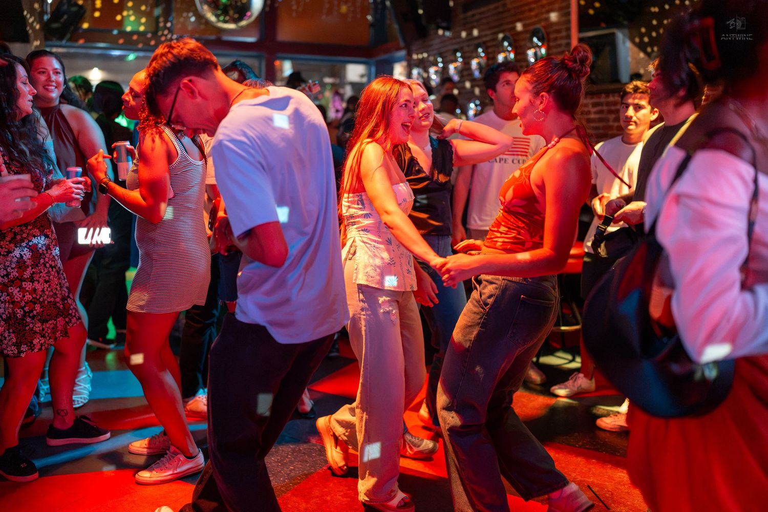 People dancing energetically at a vibrant nightclub party with red lighting and a lively crowd.