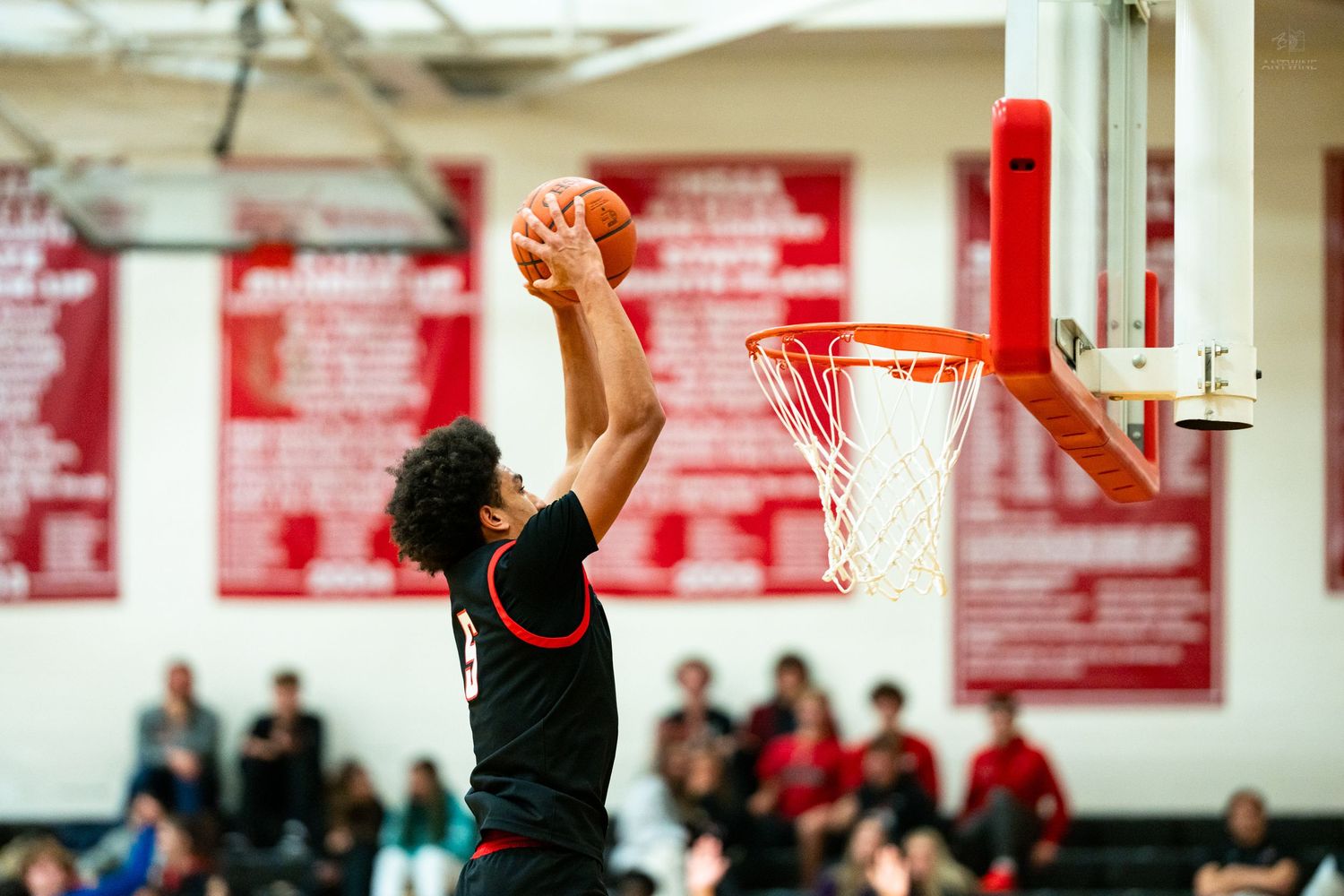 Basketball player in black uniform attempts powerful slam dunk during high school game.