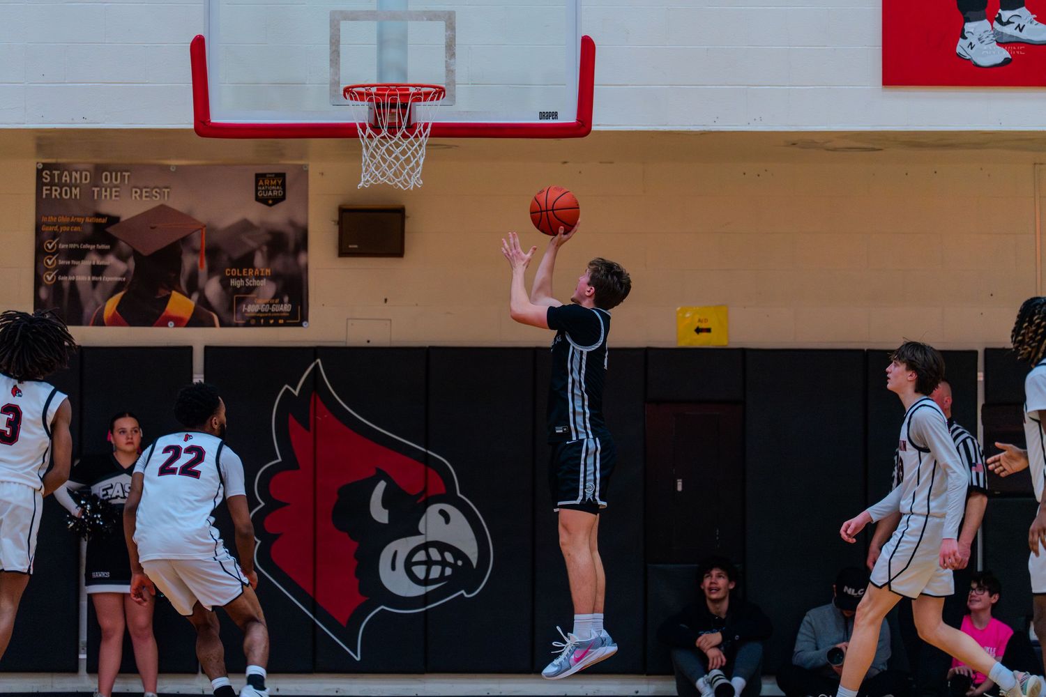 Lakers player attempts layup over Colerain defenders near Cardinals mascot logo.