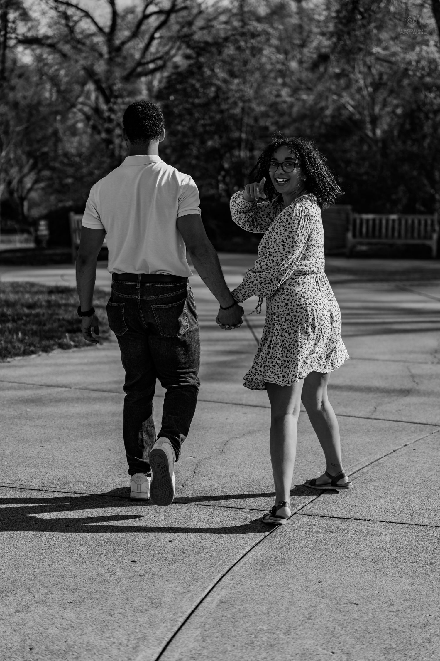 Black and white photo of a couple walking hand in hand, woman turning to smile at the camera.