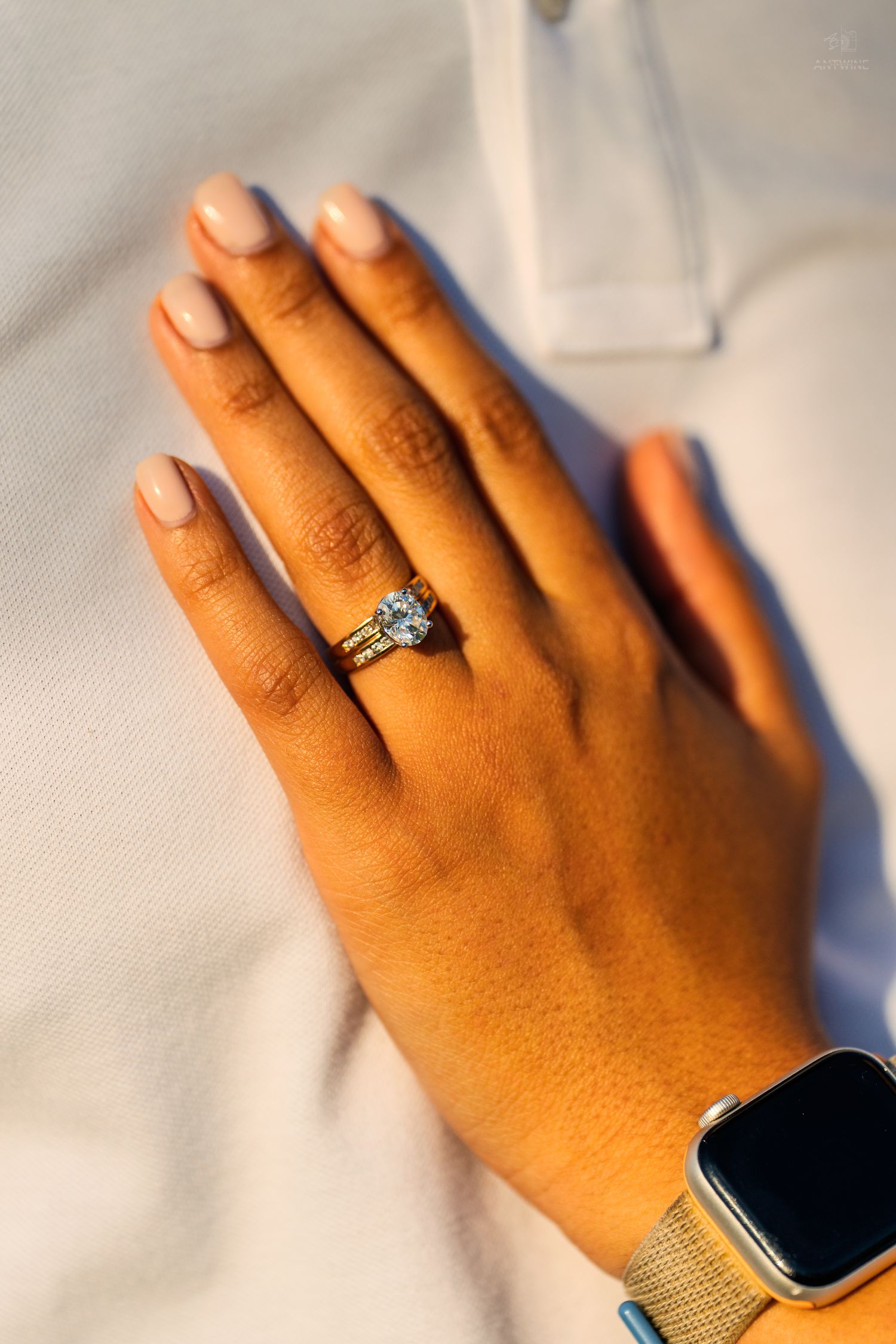 Close-up of a womans hand displaying a sparkling diamond engagement ring with gold band and Apple Watch.