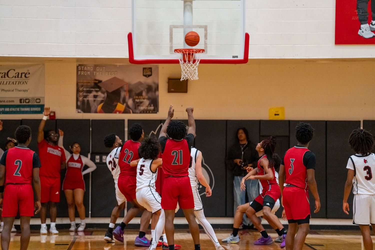 Players in red and white jerseys battle for a rebound during an intense high school basketball game.