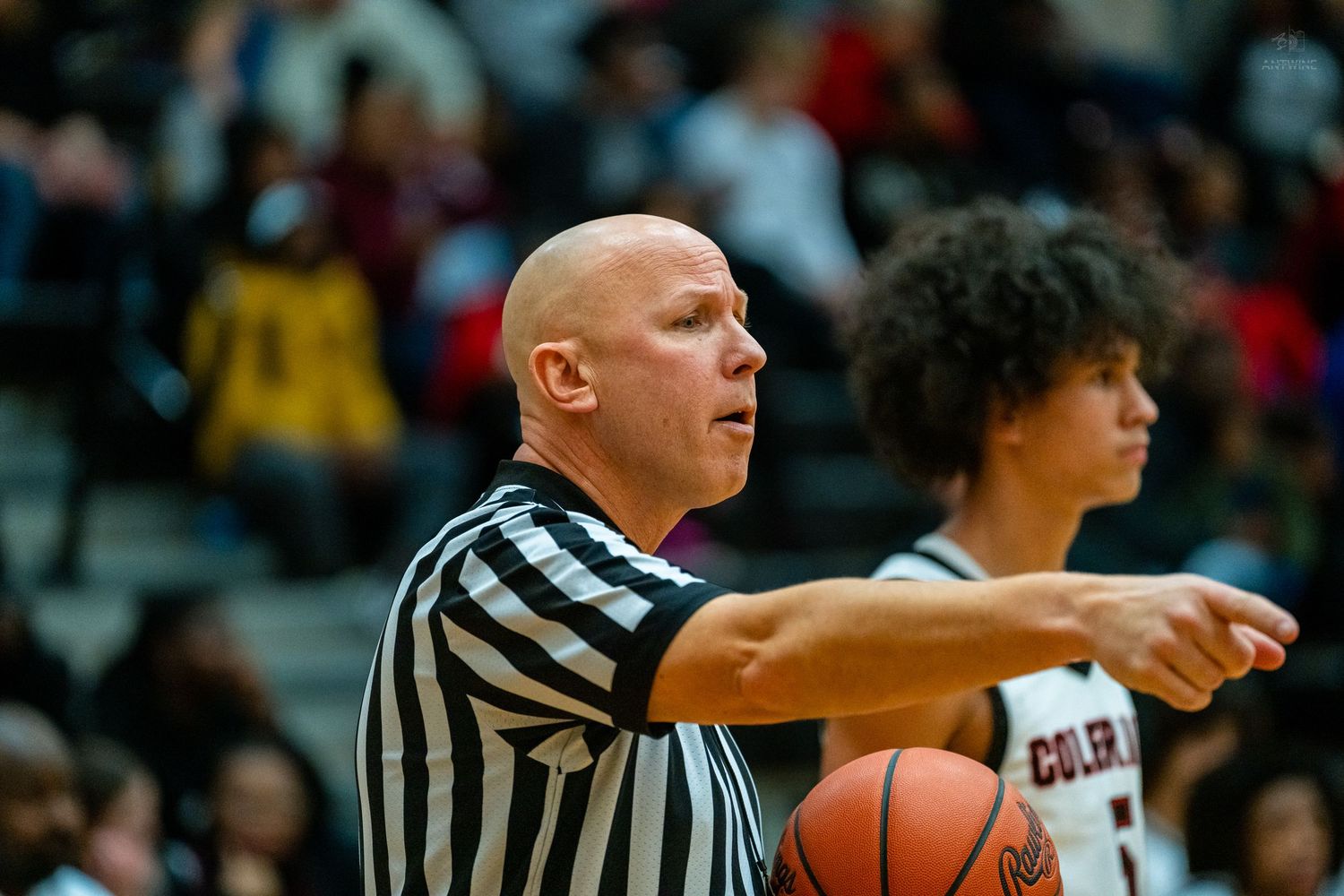 Bald basketball referee points while player #12 stands nearby on court.
