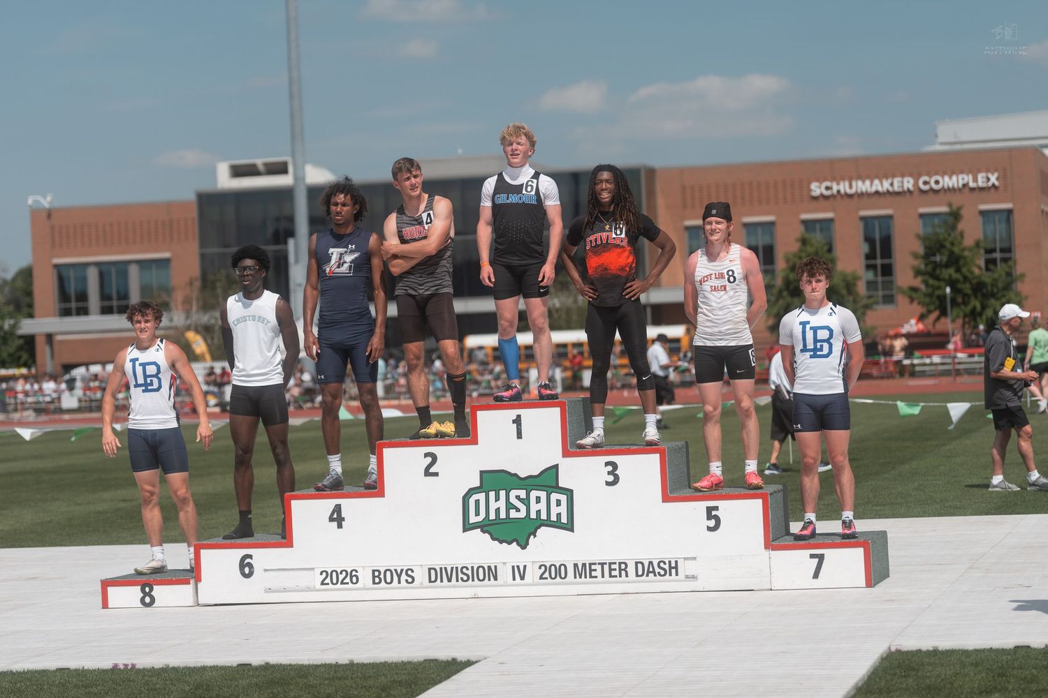 Male athletes pose on the OHSAA Boys Division IV 200 Meter Dash championship podium at an outdoor meet.
