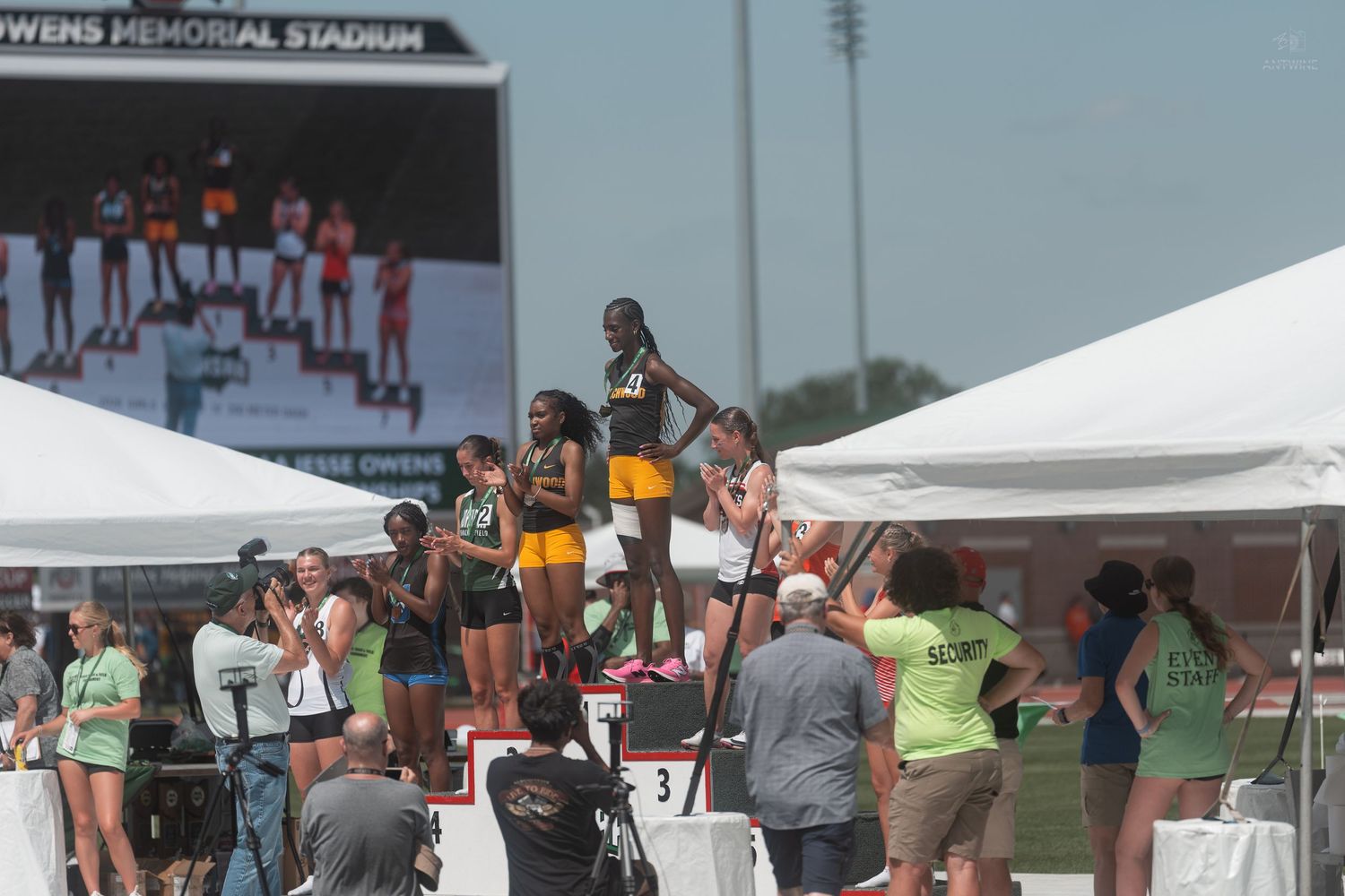 Female athletes stand on a podium at Owens Memorial Stadium during a track and field awards ceremony.