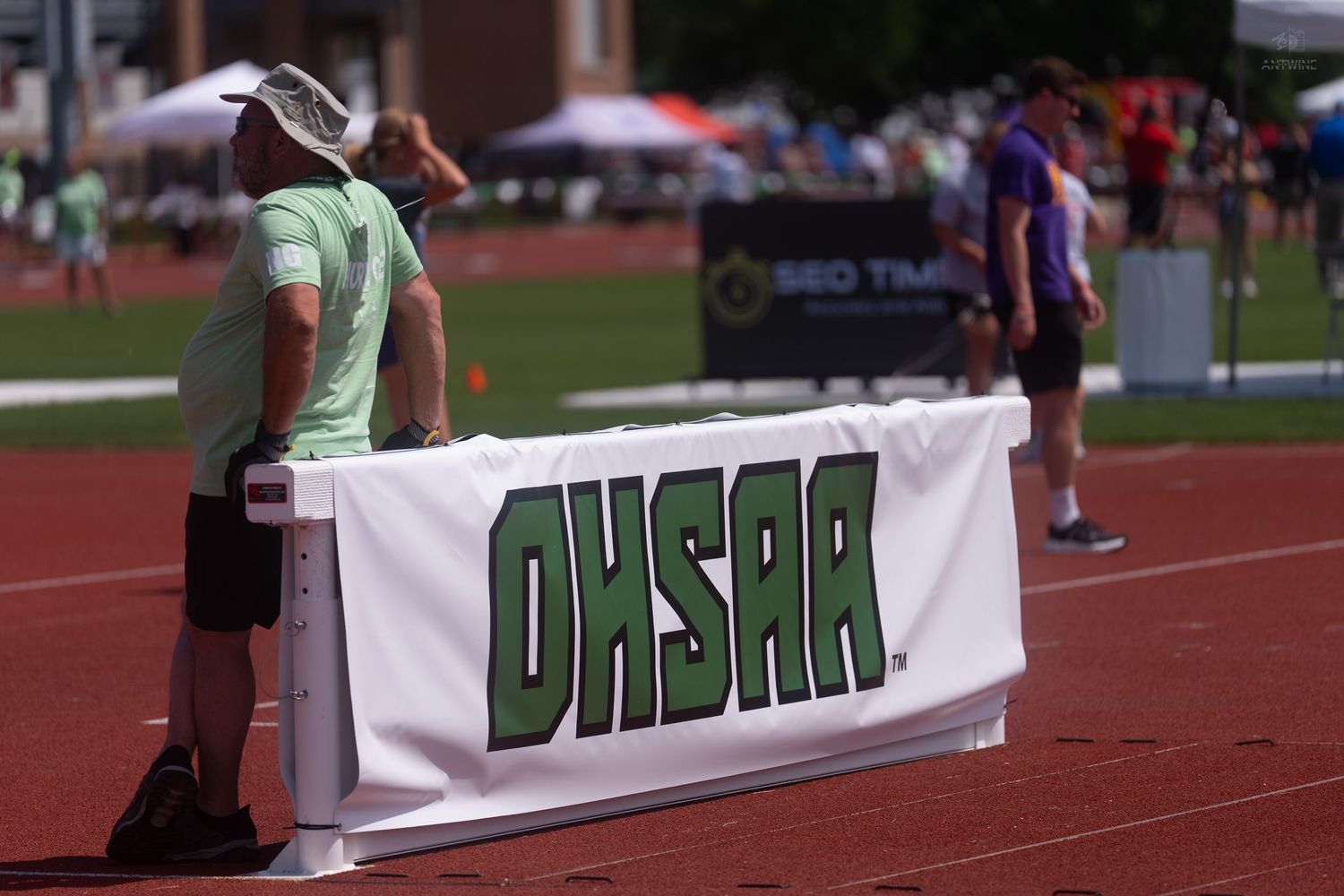 An official stands beside an OHSAA branded banner at an Ohio high school athletic association track meet.