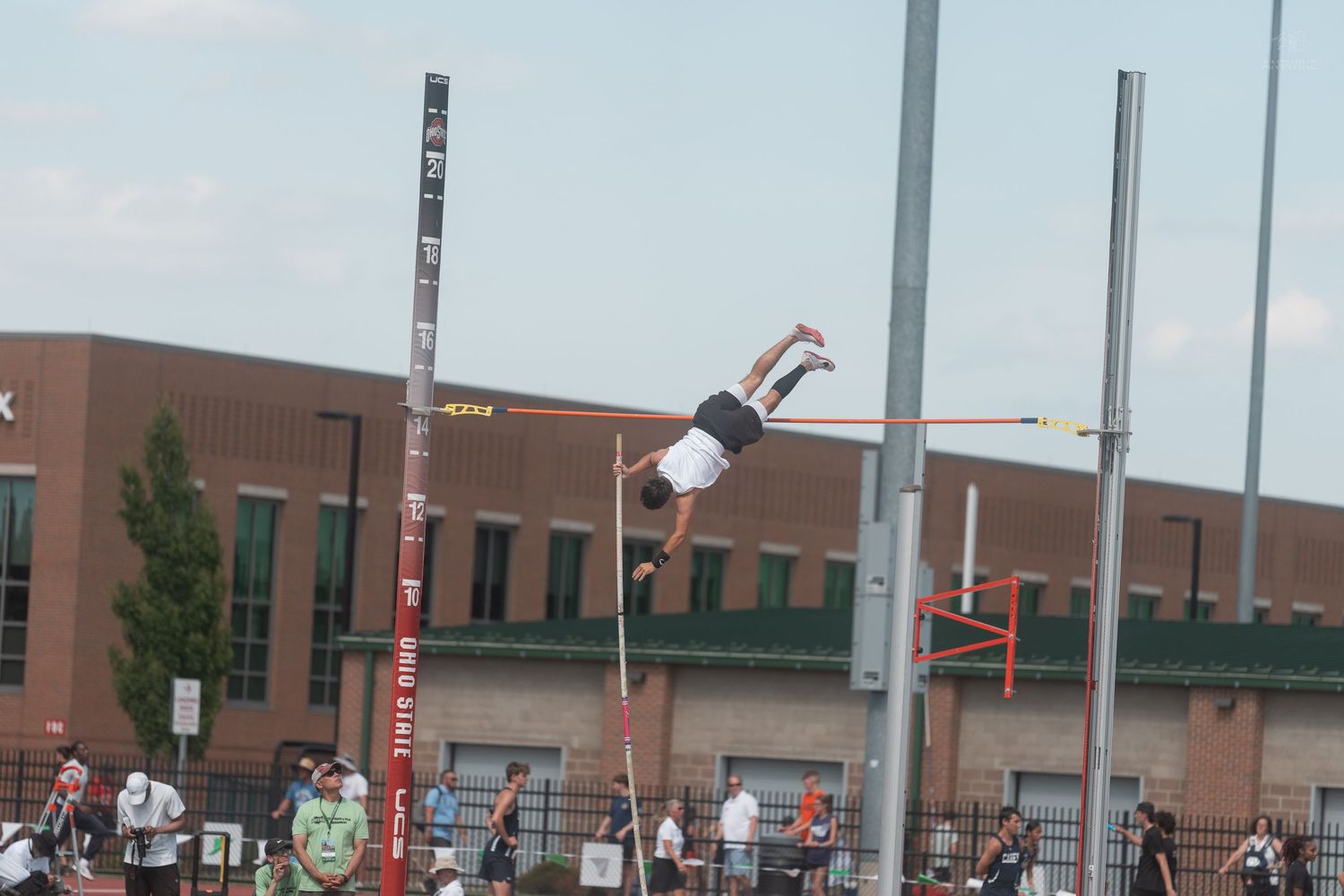 Pole vaulter clears the bar in an inverted position during an outdoor high school track and field meet.