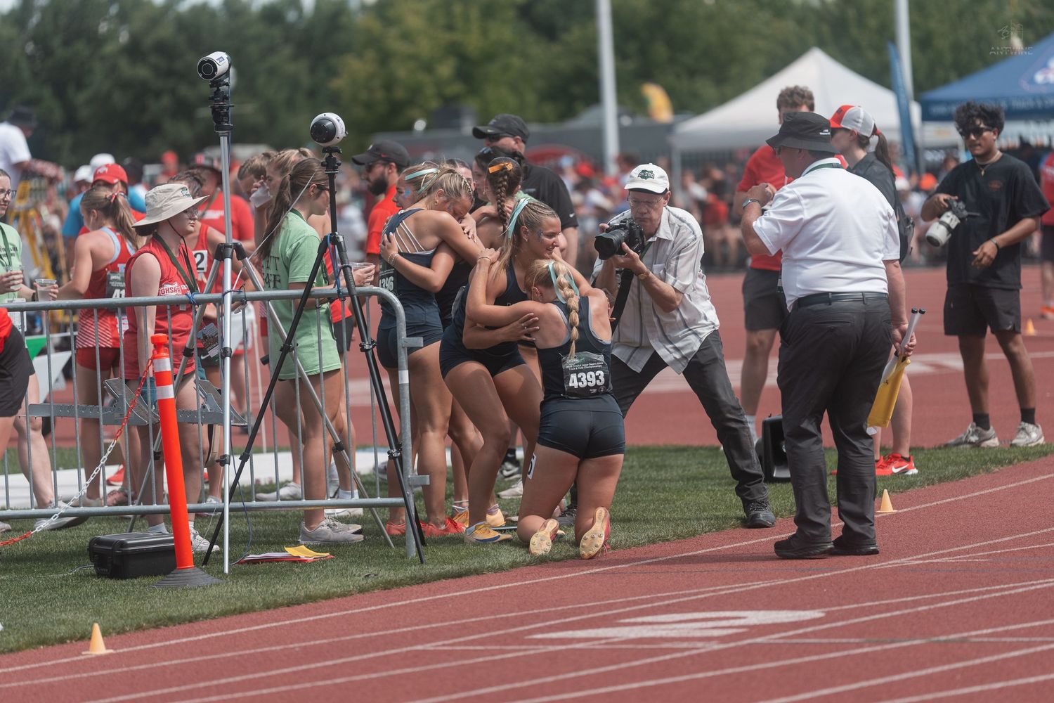 Female track athletes in dark uniforms hugging and celebrating on the track after a race.