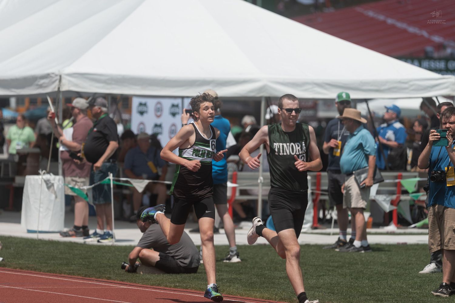 Two male runners compete in a track race wearing black uniforms at an outdoor athletic championship meet.