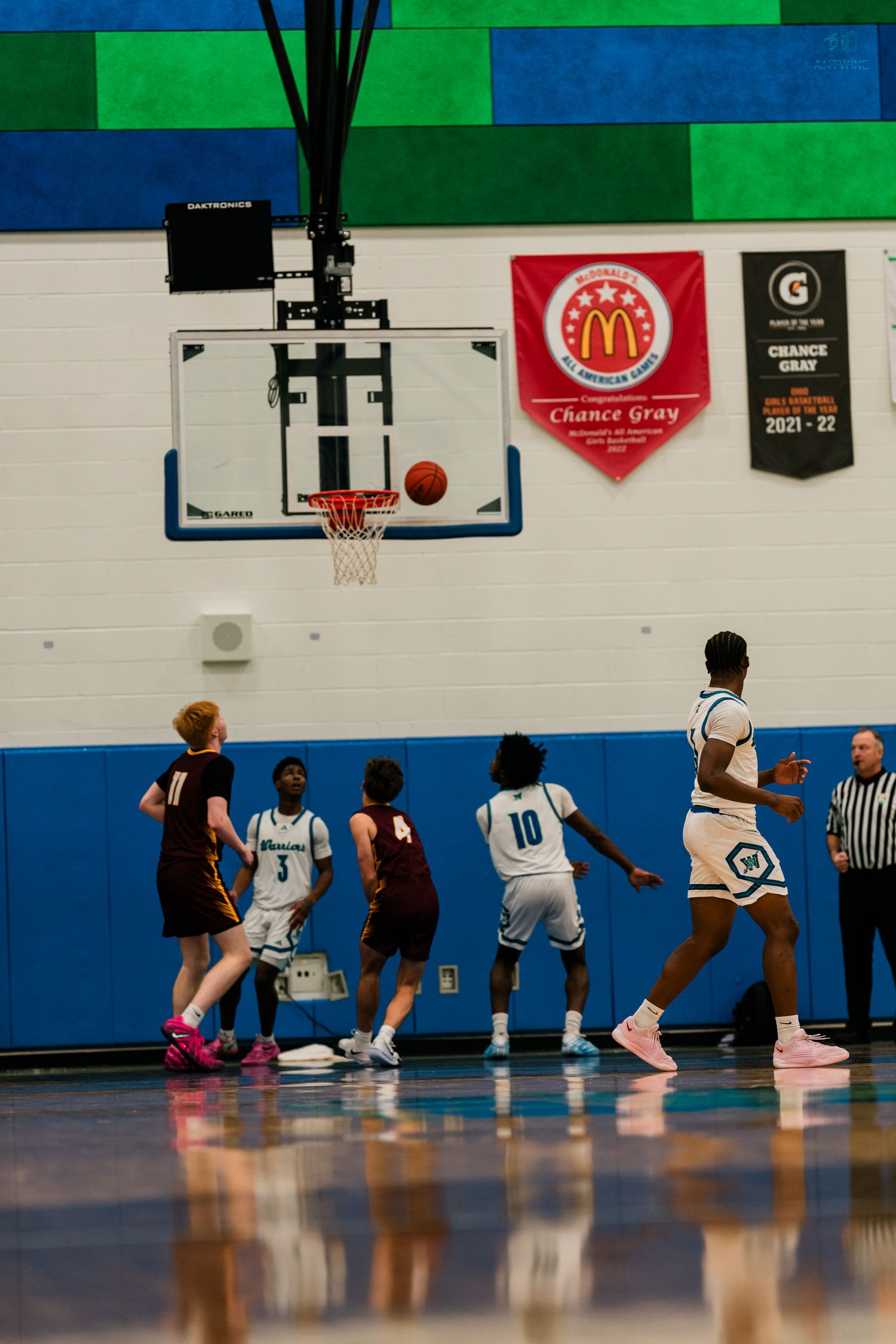 Players in maroon and white compete for a rebound under the basket during a high school basketball game.
