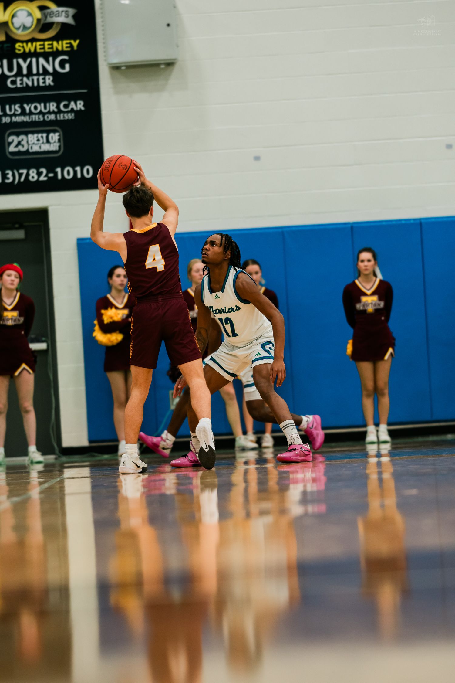 Warriors basketball player defends against maroon-jersey opponent holding ball near the three-point line.