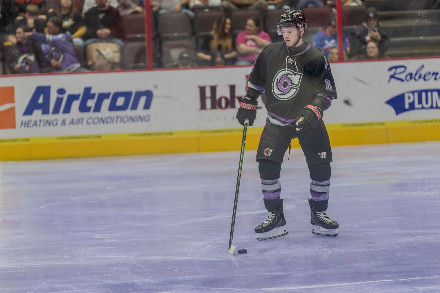 Hockey player in dark jersey skating with the puck on ice during a professional hockey match.