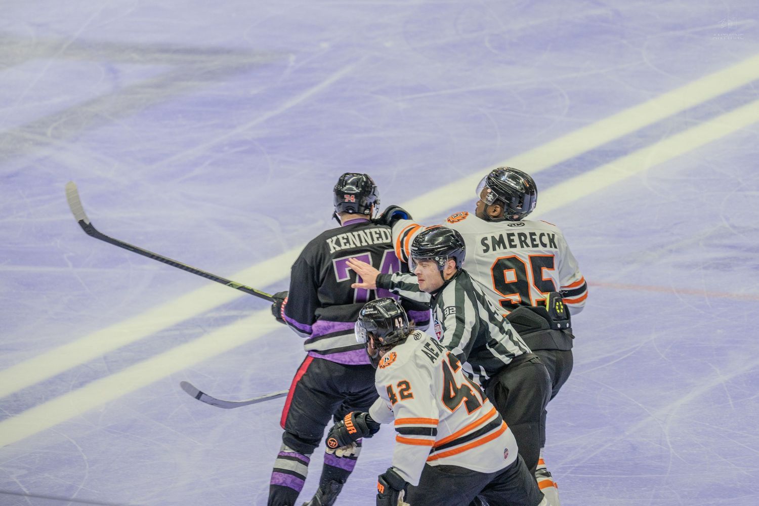 Ice hockey players Kennedy and Smereck compete near center ice with referee intervening.