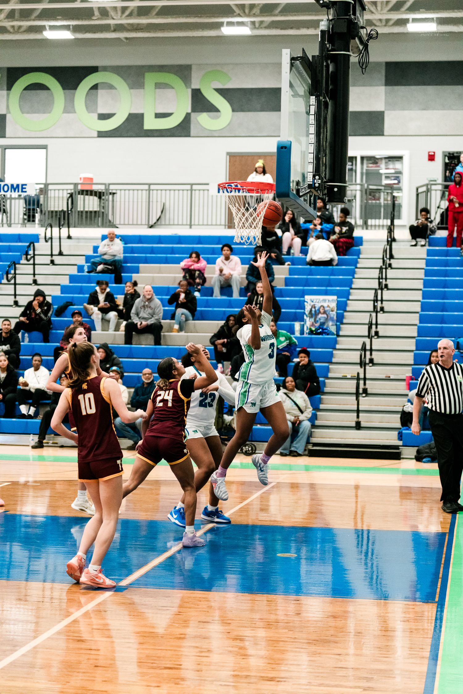 Girls high school basketball player in teal number 3 jersey attempts a layup against maroon-uniformed opponents near the basket.