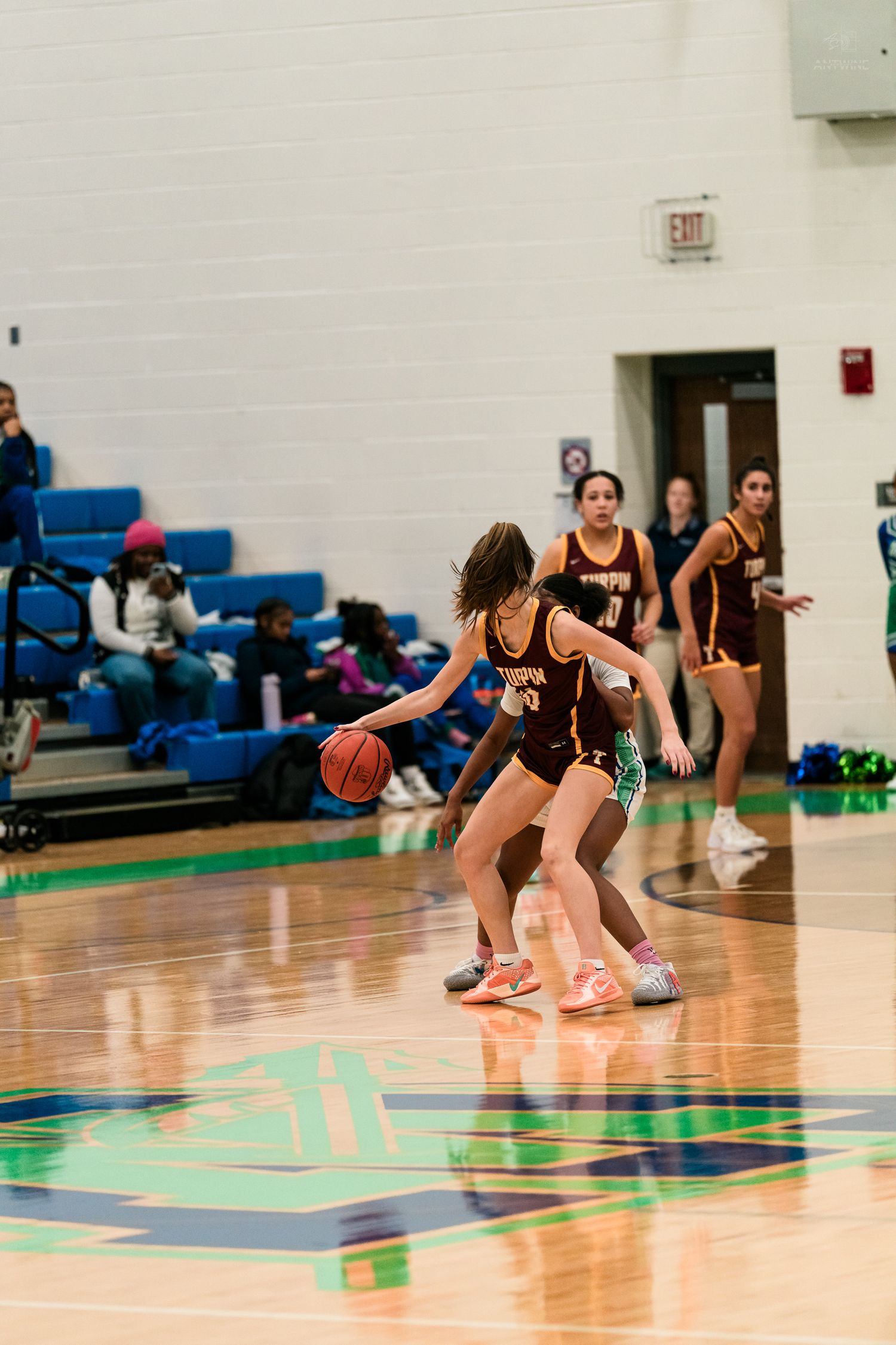 A maroon-uniformed girls basketball player dribbles while being guarded closely during a high school game.