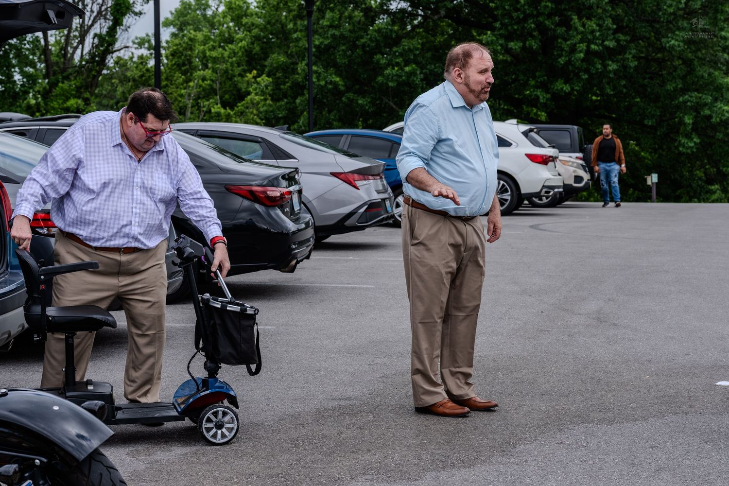 Two men in business casual attire standing in a parking lot near a mobility scooter.
