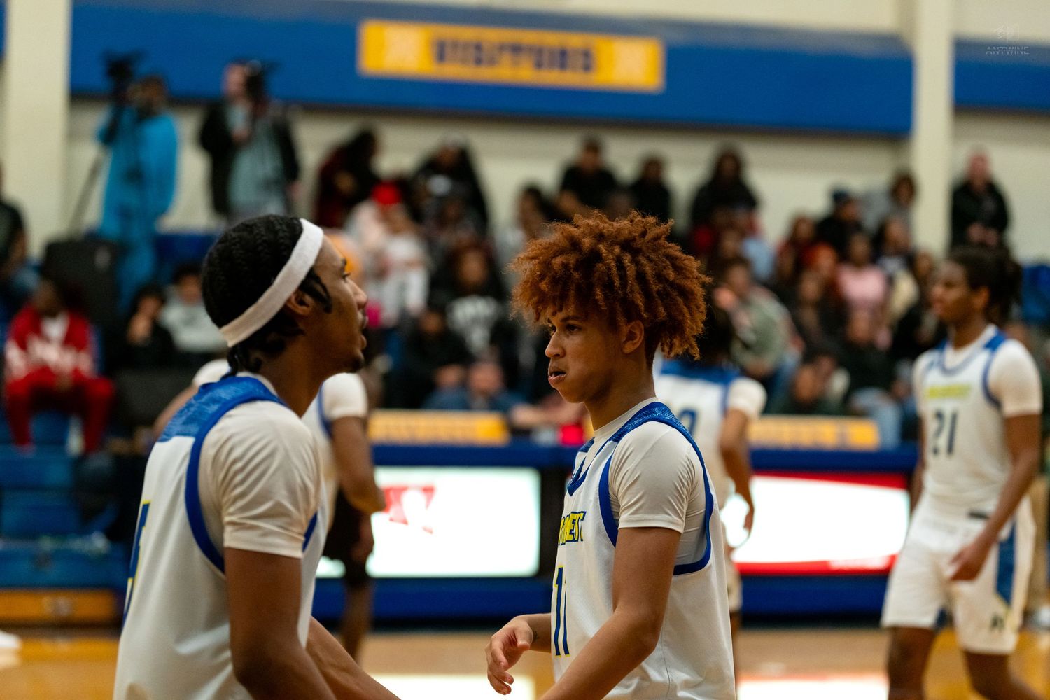 Two high school basketball players in white uniforms communicate on the court during a game.