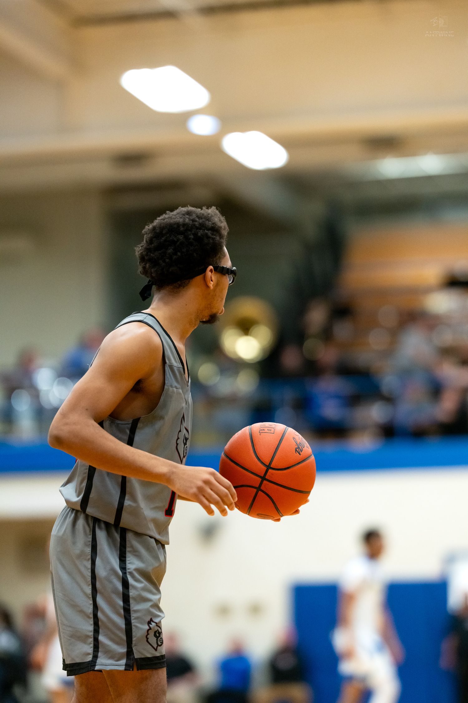 High school basketball player in gray uniform holds ball on court during competitive game.