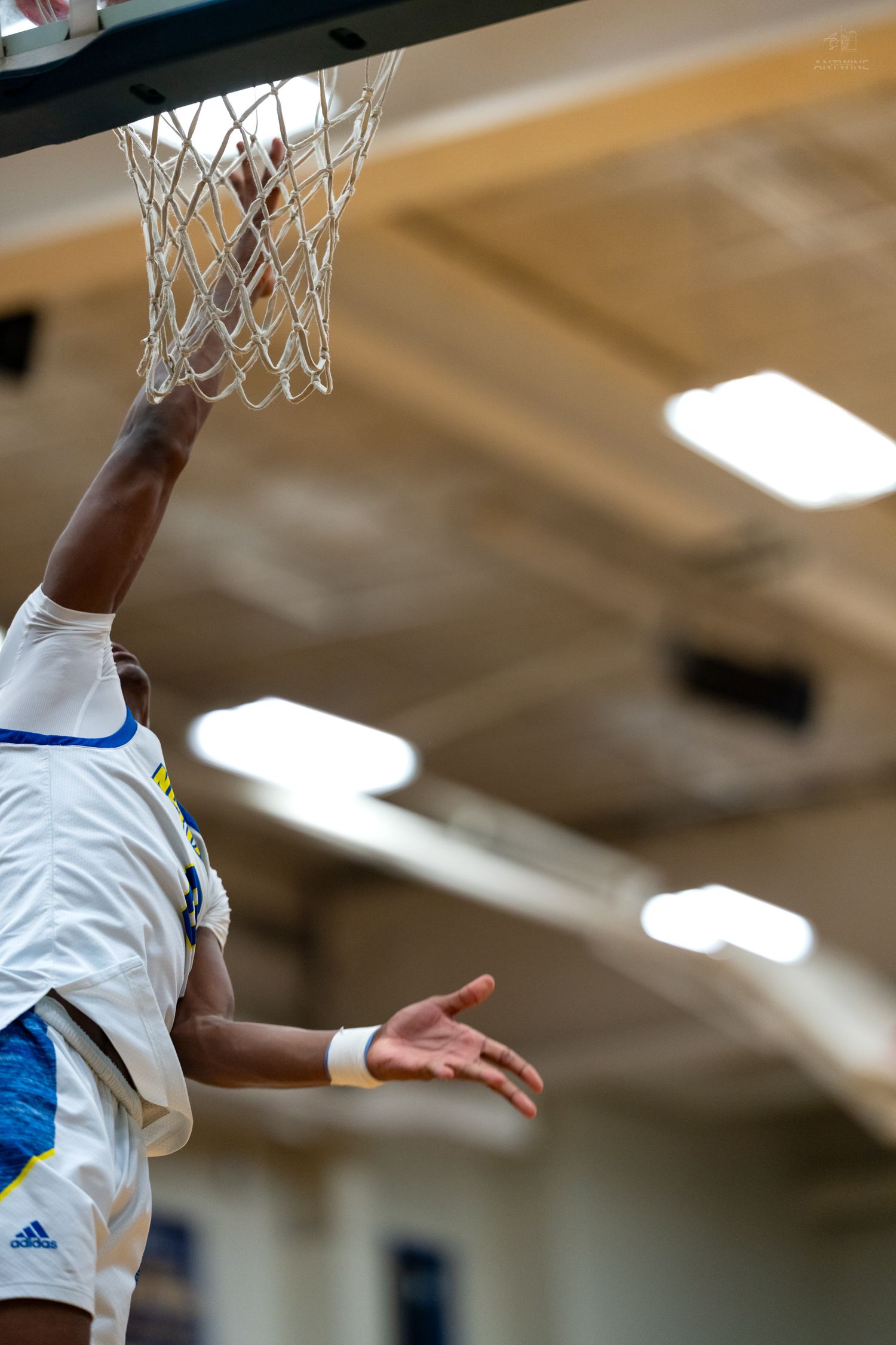 Basketball player in white Adidas jersey dunking through a white net hoop in an indoor gym.
