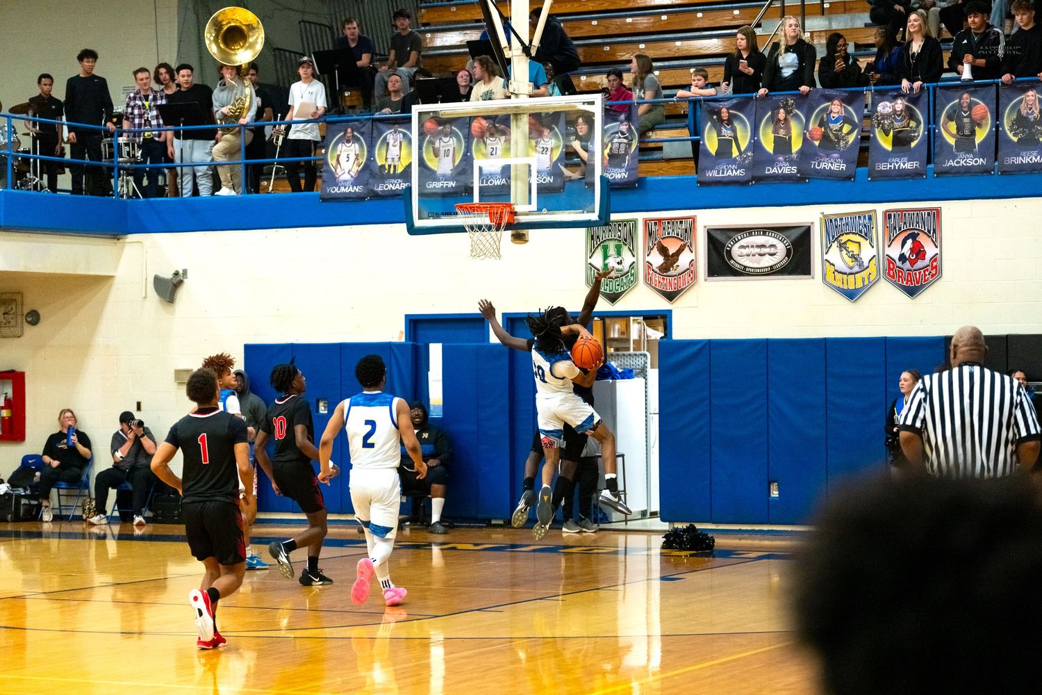 Basketball player attempts layup in packed high school gymnasium with band visible in upper level balcony.